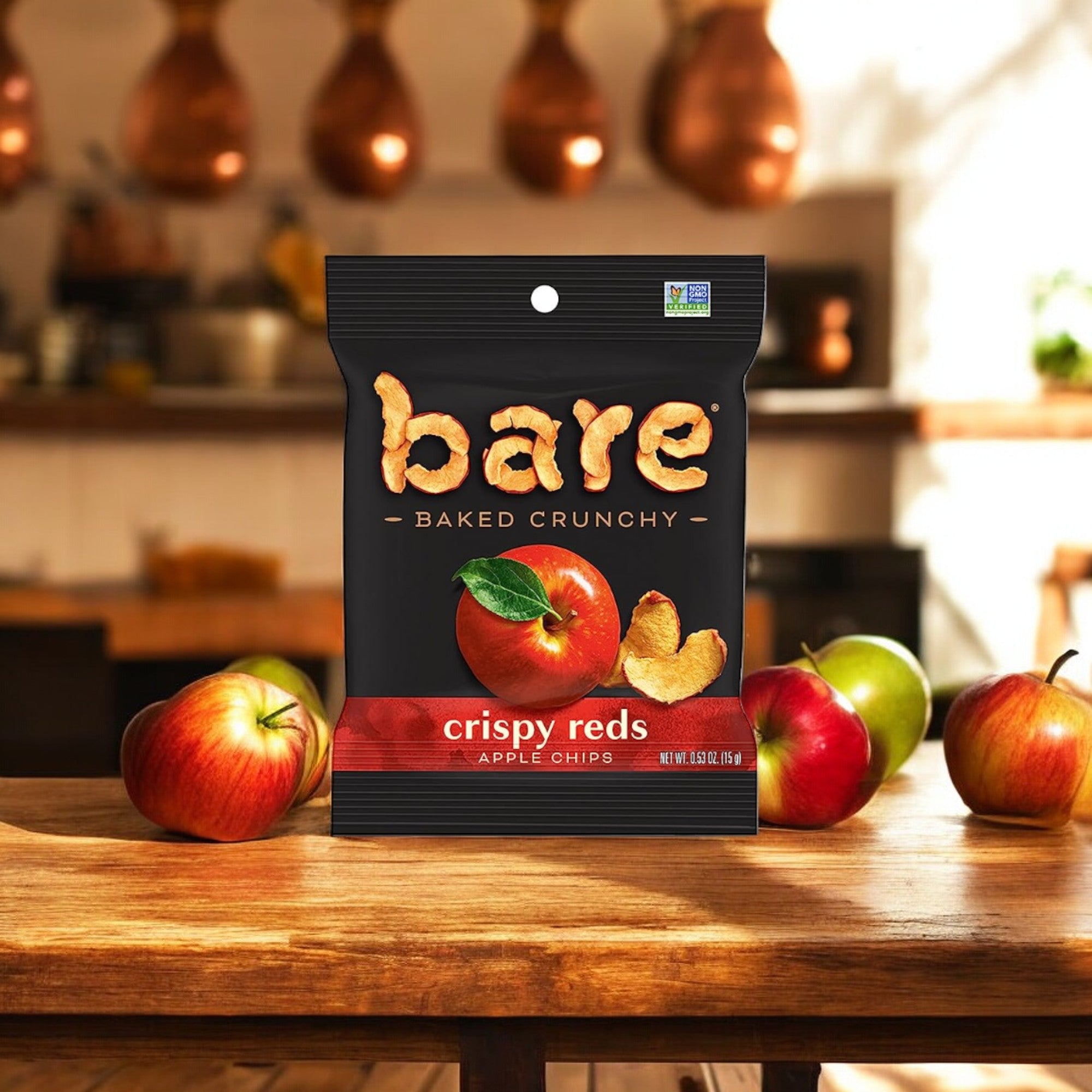 A bag of Easy Lunches Bare Baked Crunchy Crispy Red - Apple Flavor, 0.53 oz., 1 Count, sits on a wooden table surrounded by fresh apples in a cozy kitchen setting, presenting the perfect healthy snack.