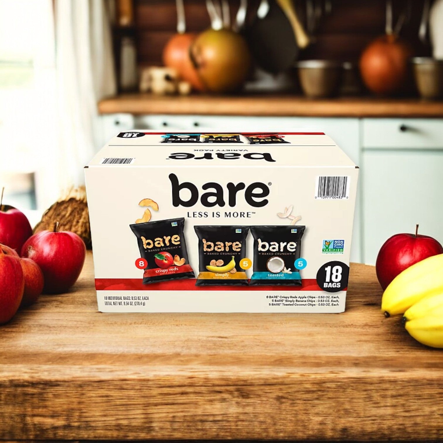 A box of Easy Lunches Bare Baked Crunchy Variety Pack Chips, containing 18 bags of 0.53 oz. each, sits on a kitchen counter surrounded by apples and bananas. This healthier snacking option features three flavors: apple chips, banana chips, and coconut chips.