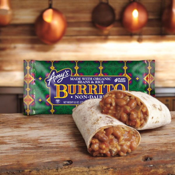 A packaged Amy's Vegan Gluten Free Non-Dairy Bean & Rice Frozen Burrito, made with organic ingredients and weighing 5.5 oz, is displayed on a wooden surface with pots hanging in the background. The burrito from Amy's, cut in half, reveals a filling of beans and rice. This convenient microwave meal is perfect for those who enjoy gluten-free and vegan burritos.