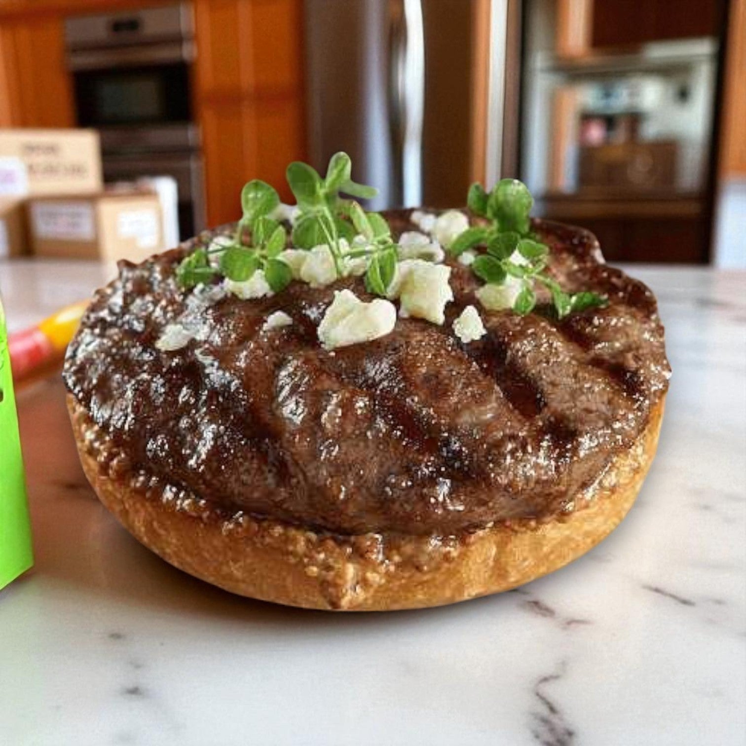 An open-faced burger patty made from Restaurant Depot's Snake River Farms Beef Eye Kalbi – American Kobe Black, topped with white cheese crumbles and microgreens on a bun, set on a marble countertop in a kitchen.