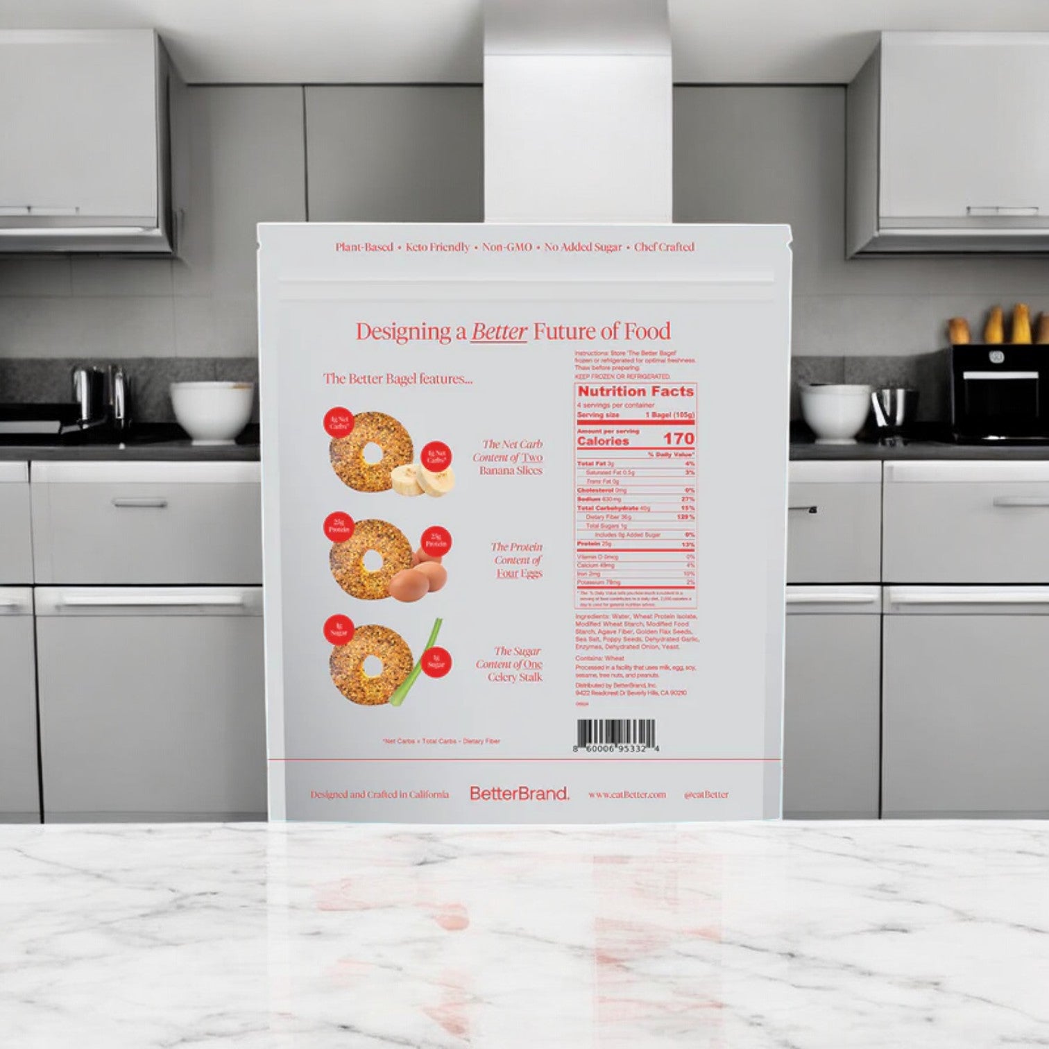 The image displays a package of BetterBrand's The Everything Better Bagel on a kitchen counter. The back of the package features images of bagels, nutrition facts, and product highlights, offering a savory blend that enhances your breakfast experience.