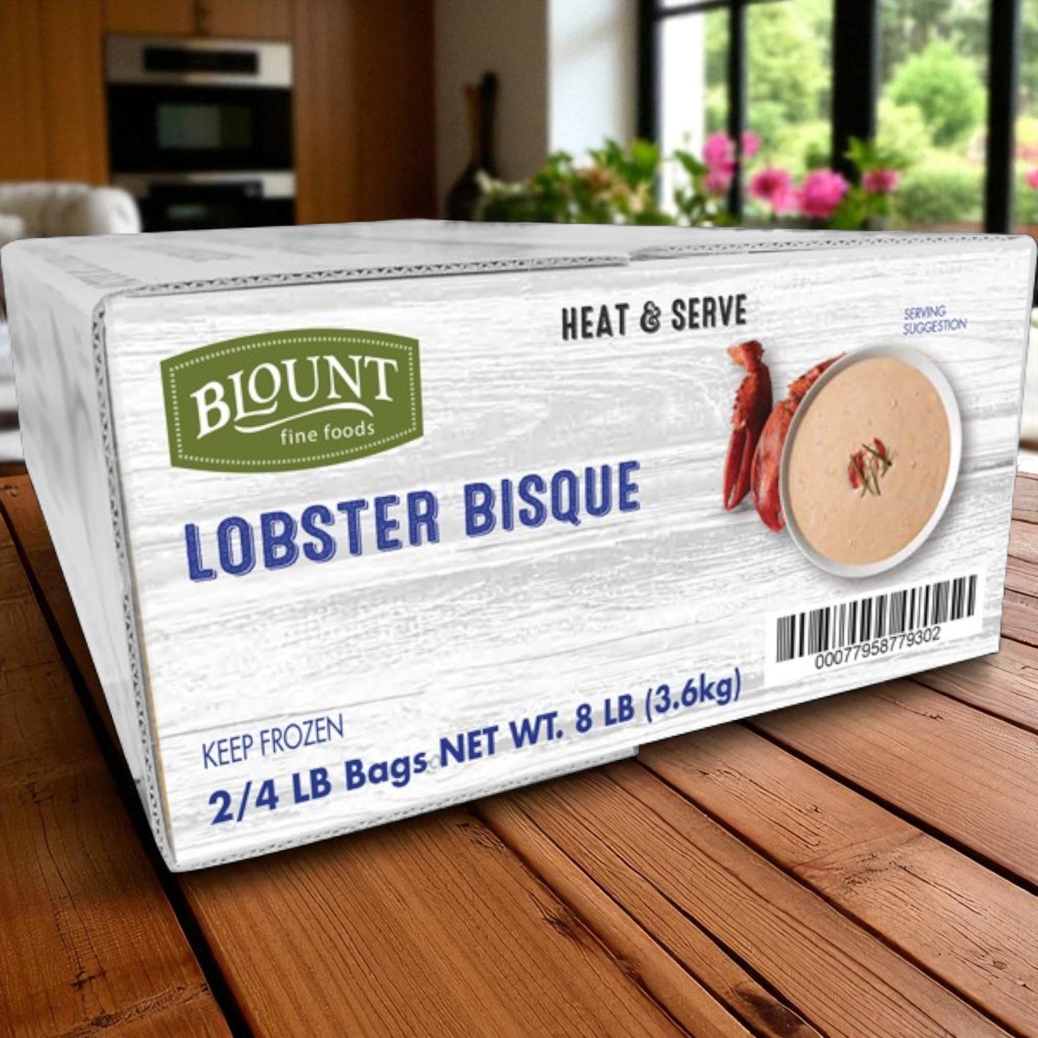 A box of Blount Fine Foods Frozen Lobster Bisque – 2 packs, 4 lbs each – labeled "Heat & Serve," rests on a kitchen table, offering restaurant-quality, rich and creamy gourmet bisque you can enjoy at home.