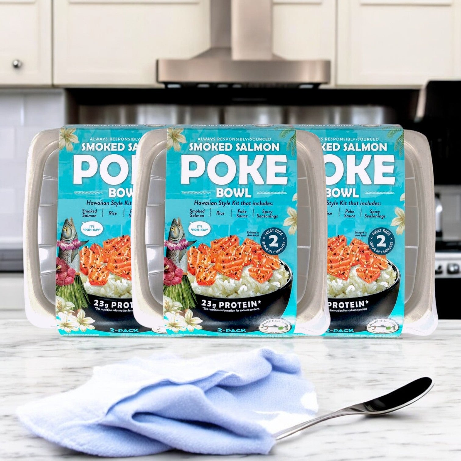 Three packs of Blue Hill Bay Smoked Salmon Poke Bowl, 9.3 oz, are arranged on a kitchen counter with a blue cloth and spoon nearby.
