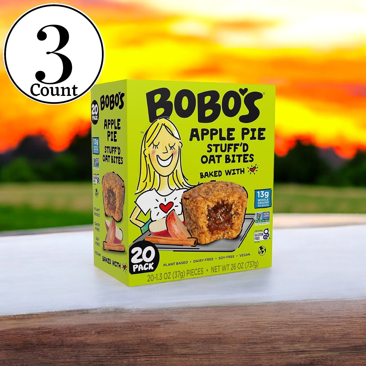 A box of Bobo's Apple Pie Filled Bites, 20 ct. -3 Box sits on a wooden surface against a sunset backdrop. This convenient snack, crafted from wholesome ingredients, features "20 ct." and "-3 Box" on its packaging, offering apple pie-filled bites ideal for any time of day.