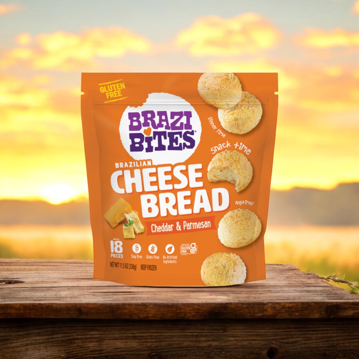 An 11.5 oz bag of Brazi Bites Cheddar & Parmesan Brazilian Cheese Bread is placed on a wooden surface with a sunset backdrop.