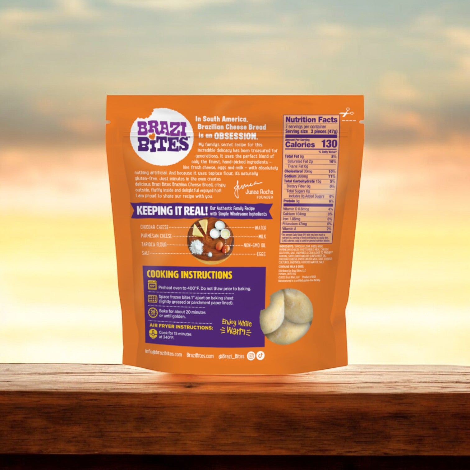 The back view of the Brazi Bites Cheddar & Parmesan Brazilian Cheese Bread package showcases product information, cooking instructions, and nutritional details. This Cheddar & Parmesan flavor is clearly marked as Gluten-Free. The 11.5 oz package rests on a wooden surface with a softly blurred background.