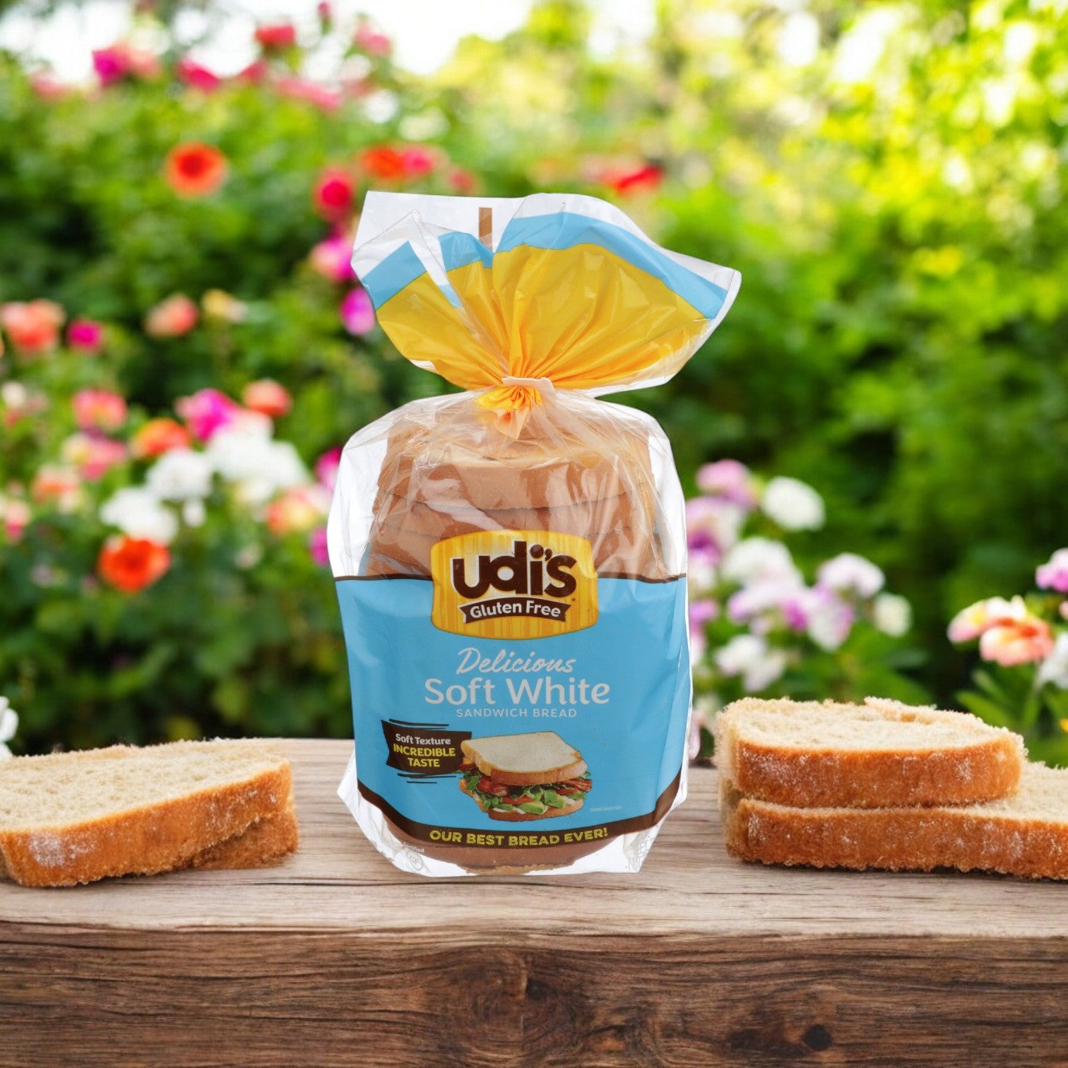 A loaf of Udi's Bread White Soft Sandwich Gluten Free (24 oz. - 1 Count) rests on a wooden surface outdoors, flanked by slices of bread and framed by a garden backdrop. Relish its versatility as the perfect soft sandwich bread, ideal for any meal in a gluten-free lifestyle.