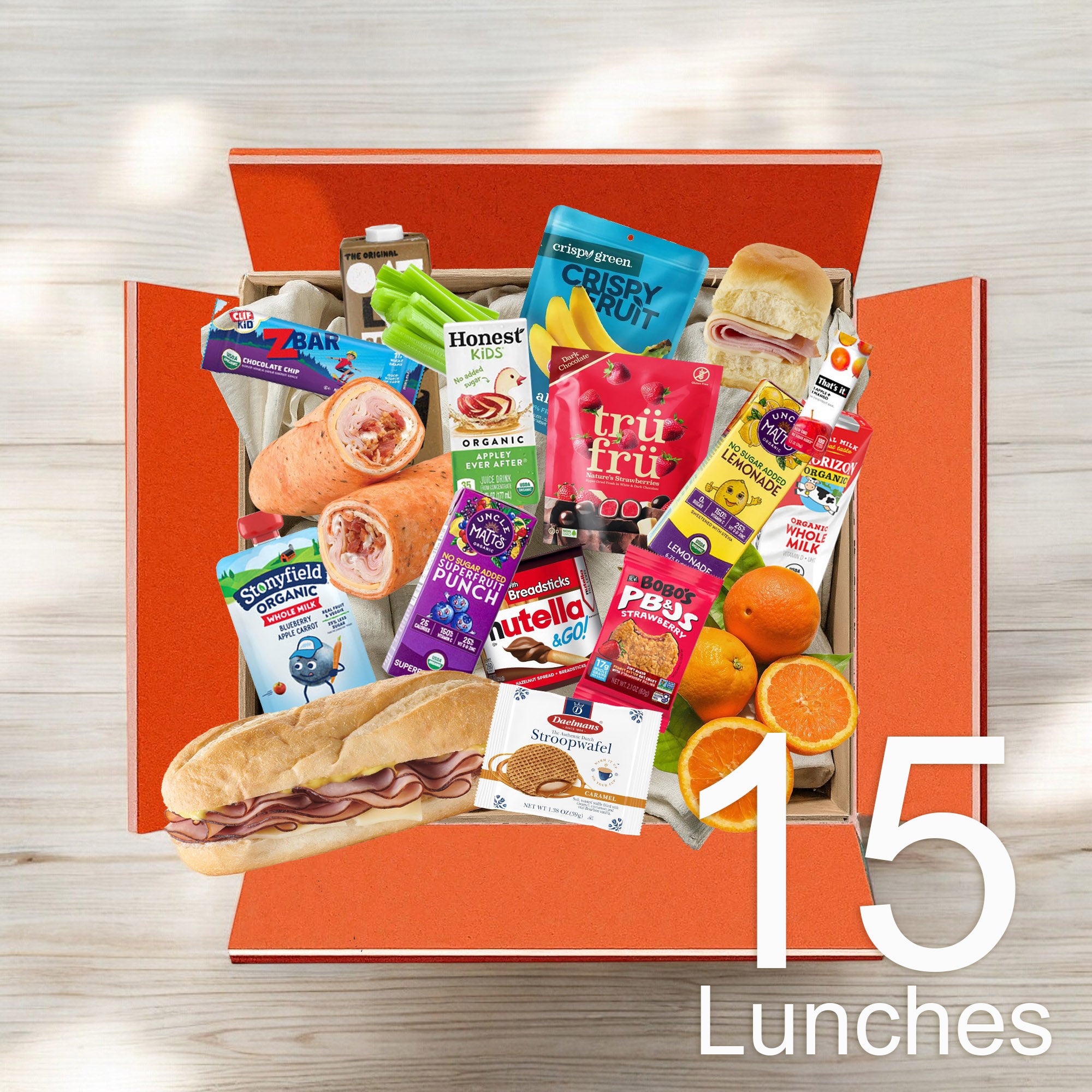 An open orange box from Easy Lunches contains a bundle of lunch items, including juice boxes, sandwiches, fruit, snacks, and packaged foods, with a label reading "Kids 15 Lunch Bundle $7.99 Per Lunch.