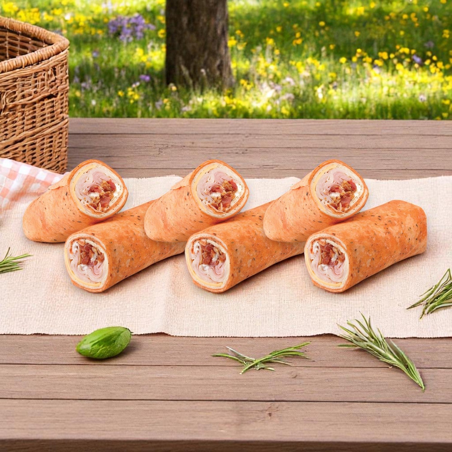 Ten assorted sandwiches from the E.A. Sween 10-Pack Sandwich Variety Bundle—Turkey Club, Chicken Caesar Wraps, and Smoked Turkey Subs—are arranged on a wooden table outdoors, with a picnic basket and greenery in the background.