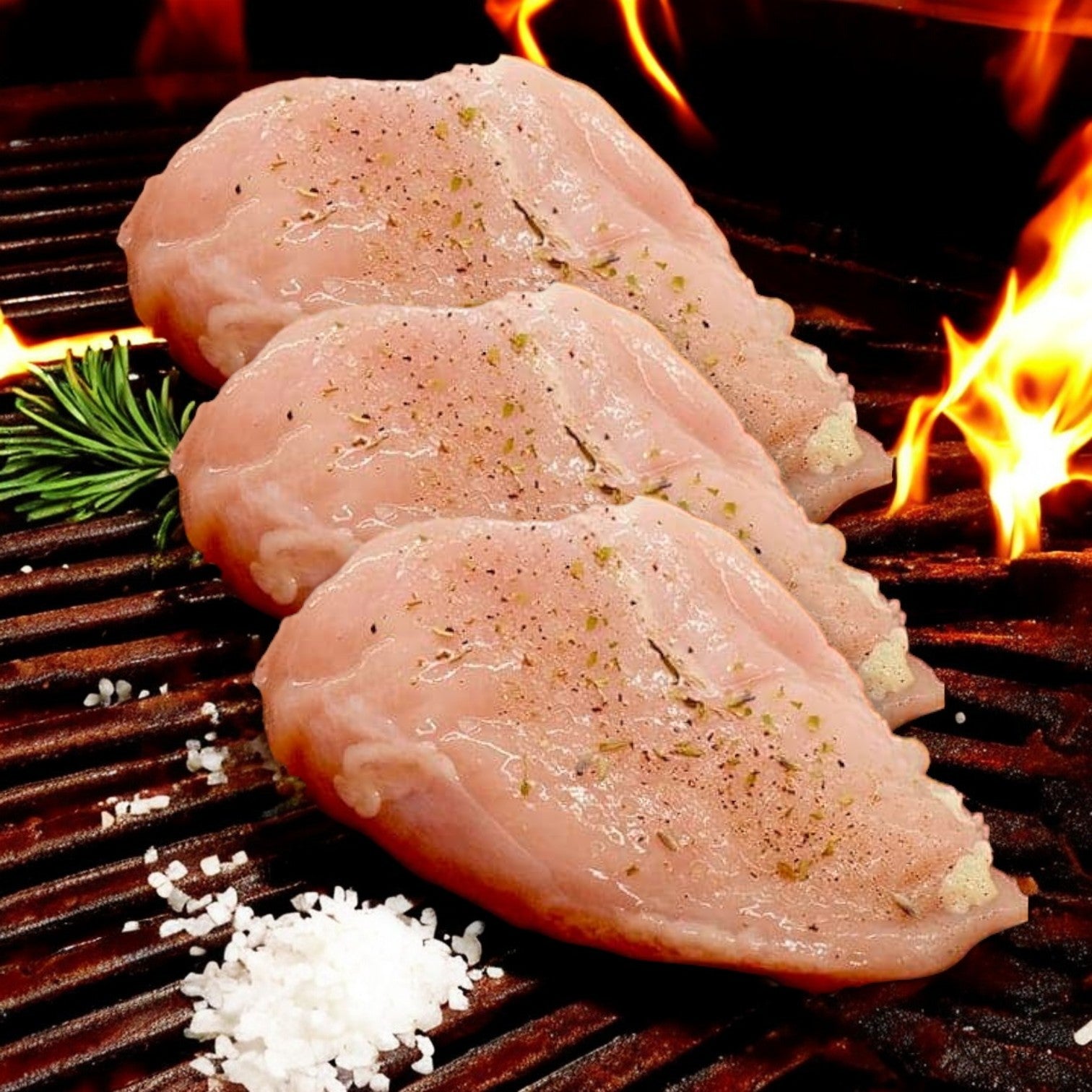 Three Mino Prime Steaks all-natural chicken breasts, seasoned with salt and pepper, sizzle on the grill as flames dance. Nearby, a sprig of rosemary adds a fragrant touch to this high-protein feast.