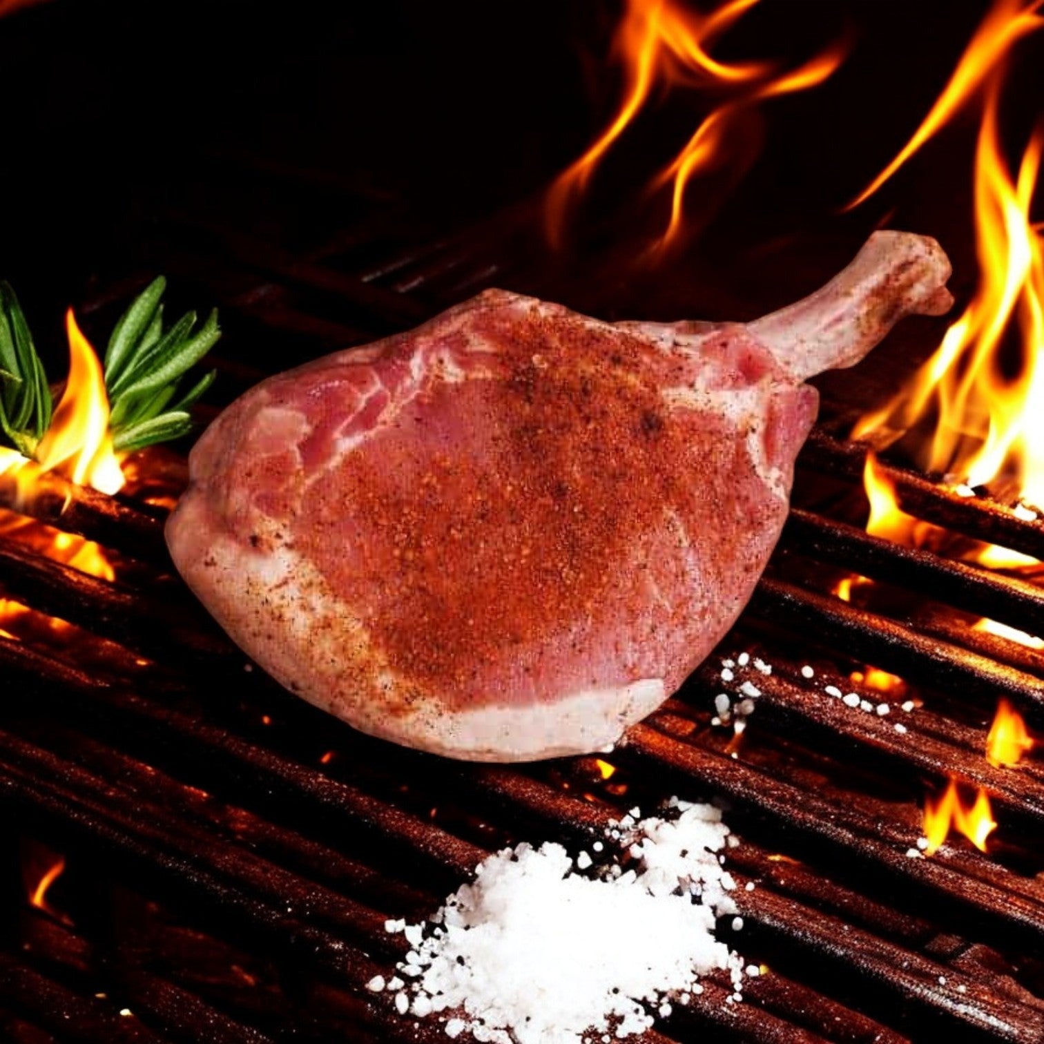 A seasoned 12 oz French Pork Chop from Mino Prime Steaks sizzles on the grill, flames flickering behind. A sprig of rosemary and a dash of salt elevate its premium quality.