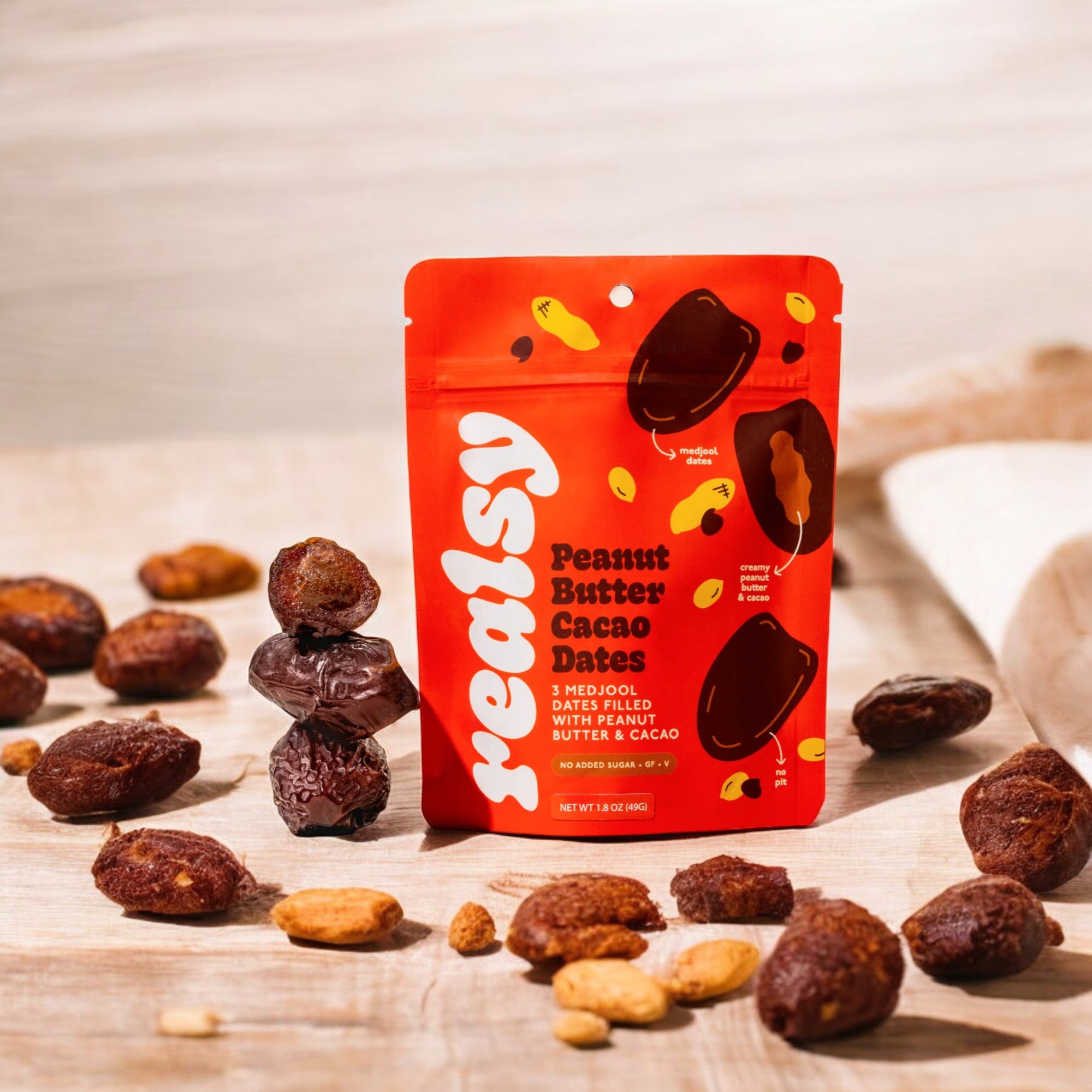 A red package of "Realsy" Cacao Peanut Butter Dates sits surrounded by medjool dates and peanuts on a wooden surface, capturing the essence of a healthy Snickers with its naturally sweet produce.