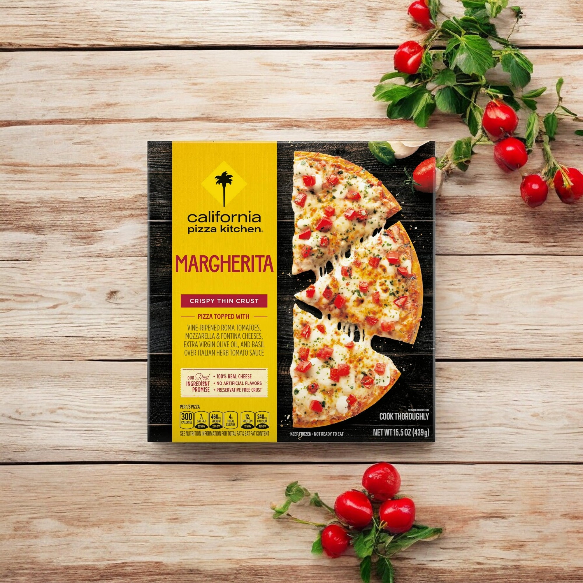 A box of California Pizza Kitchen Margherita Thin Crust - 1 Count is on a wooden table, surrounded by cherry tomatoes, fresh mozzarella cheese, and herbs.