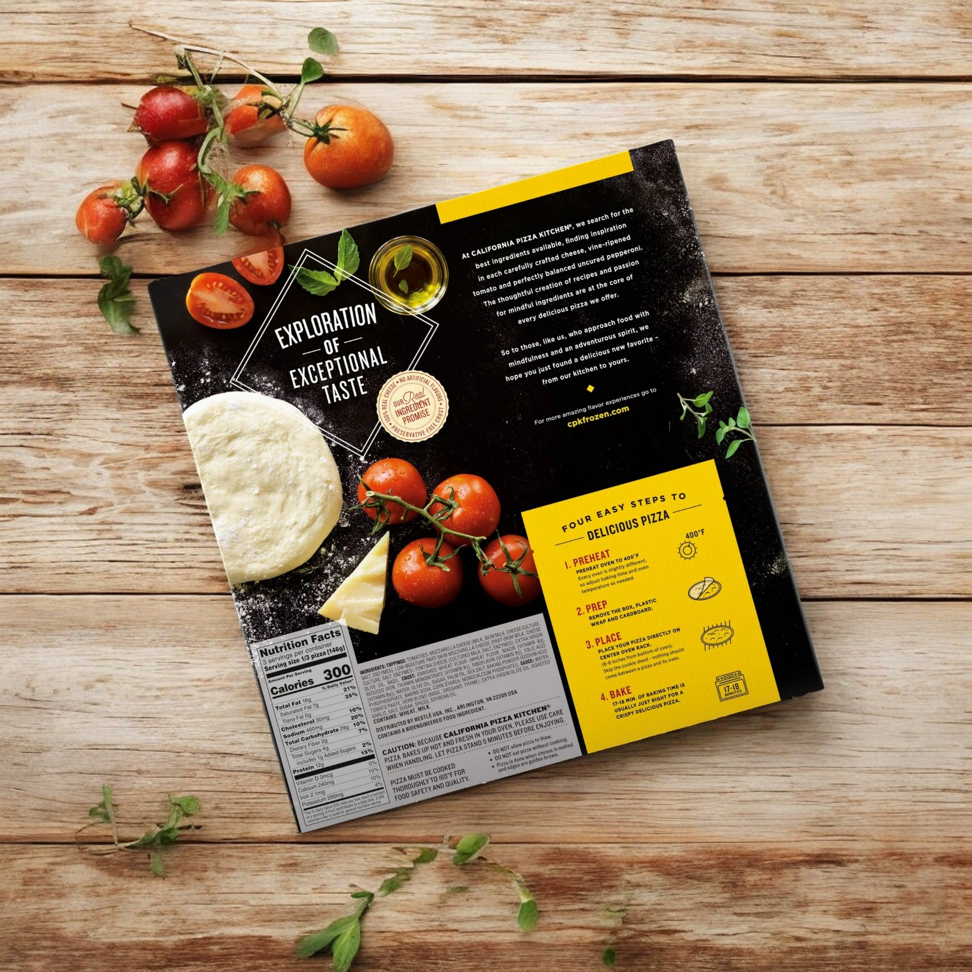 On a wooden table, the back of a California Pizza Kitchen Margherita Thin Crust - 1 Count pizza box is surrounded by scattered cherry tomatoes and basil leaves. The box includes pizza instructions, nutritional information, and promotional text boasting fresh mozzarella cheese and vine-ripened tomatoes for an authentic taste.