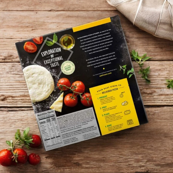 A packaged food product, labeled "California Pizza Kitchen White Thin Crust - 1 Count," sits on a wooden surface surrounded by tomatoes and herbs. The packaging, styled similarly to a California Pizza Kitchen gourmet pizza, features the text "Exploration of Exceptional Taste" along with nutritional facts and cooking instructions.