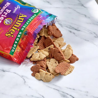 An opened bag of Annie's Organic Friends Bunny Grahams - 1 Count reveals an assortment of bunny-shaped grahams in various colors scattered on a marble surface. Enjoy these non-GMO snacks, perfect USDA Organic treats for any occasion.