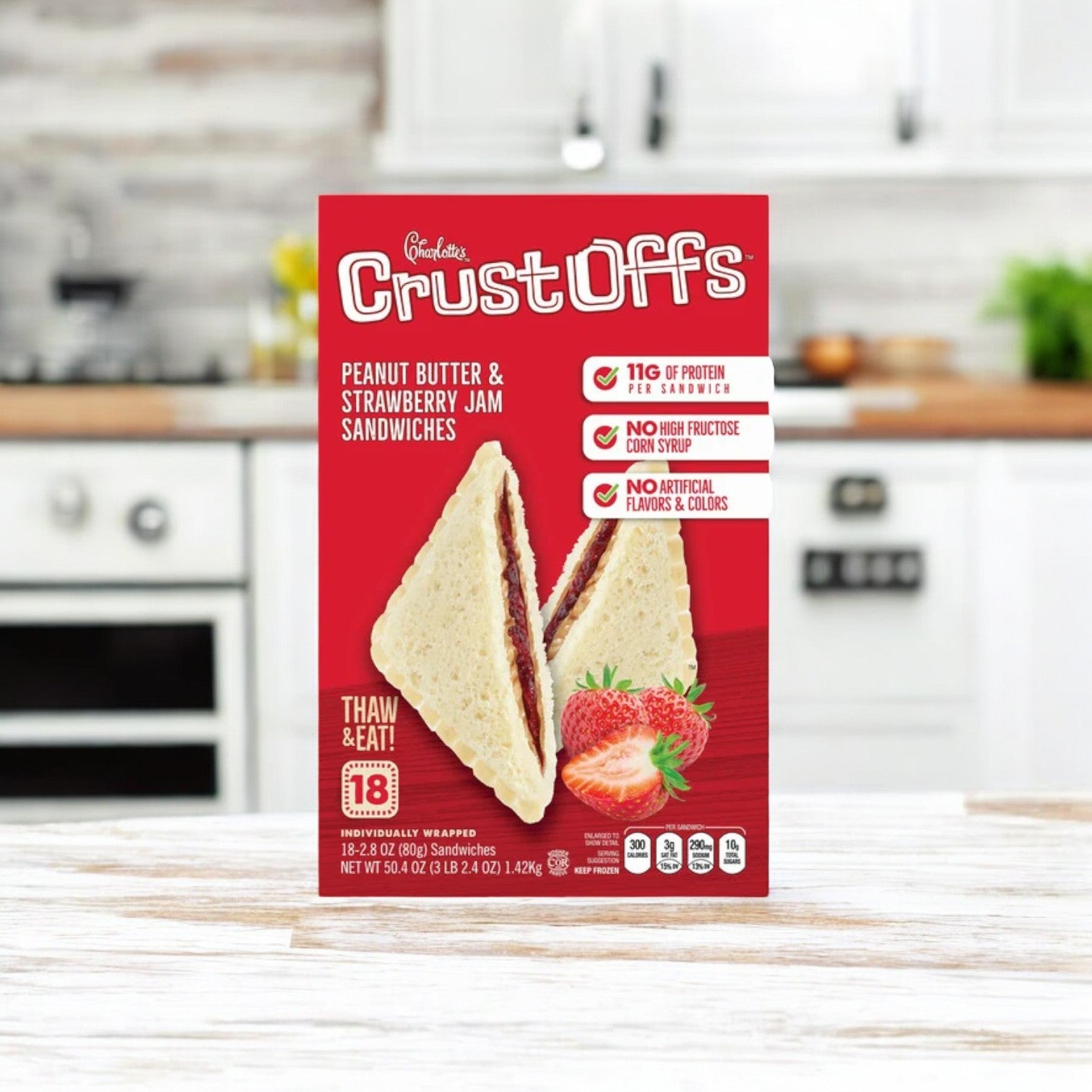 A box of Easy Lunches' Charlotte's Crust Offs sandwiches offers delicate crust-free sandwiches filled with creamy peanut butter and luscious strawberry jam, featuring 18 individually wrapped servings. Perfectly placed on a kitchen counter with a blurred background.