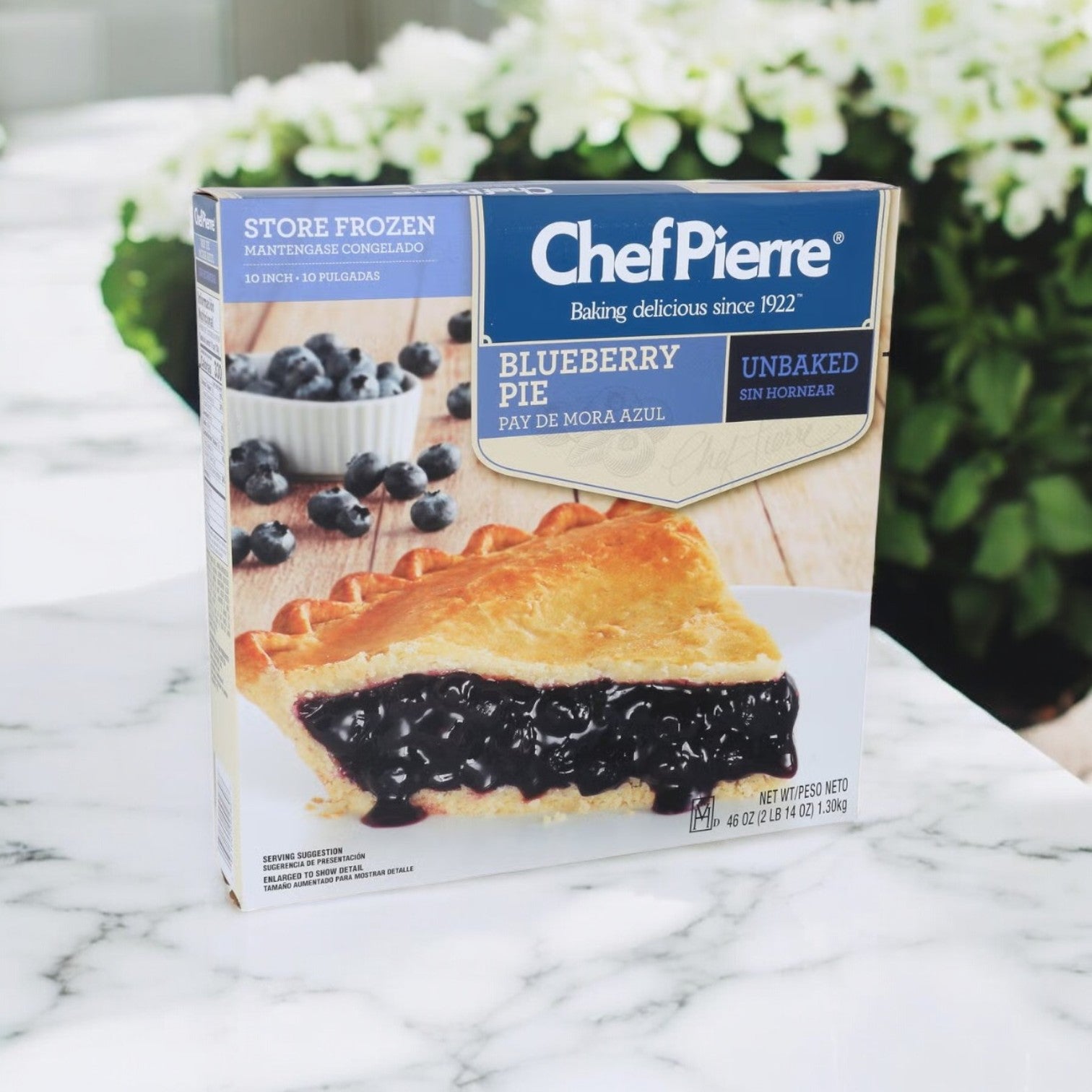 A Chef Pierre Blueberry Pie (46 oz., 3 count) brings a homemade taste, beautifully displayed on a marble surface and surrounded by green plants.