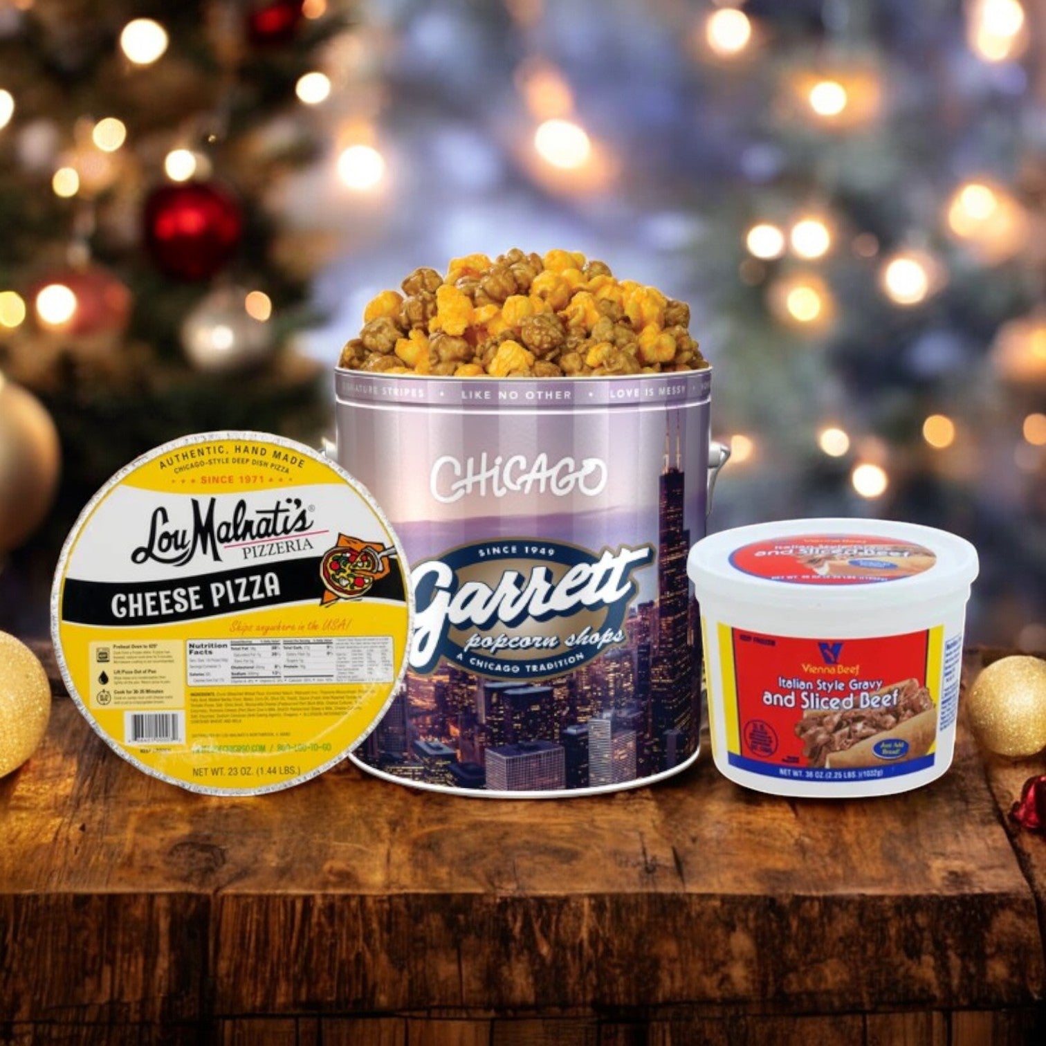 A cheese pizza, Chicago's 3 Pack Sampler of Garrett popcorn from Easy Lunches, and a container of Italian sliced beef are displayed on a wooden table, with festive lights and decorations in the background.