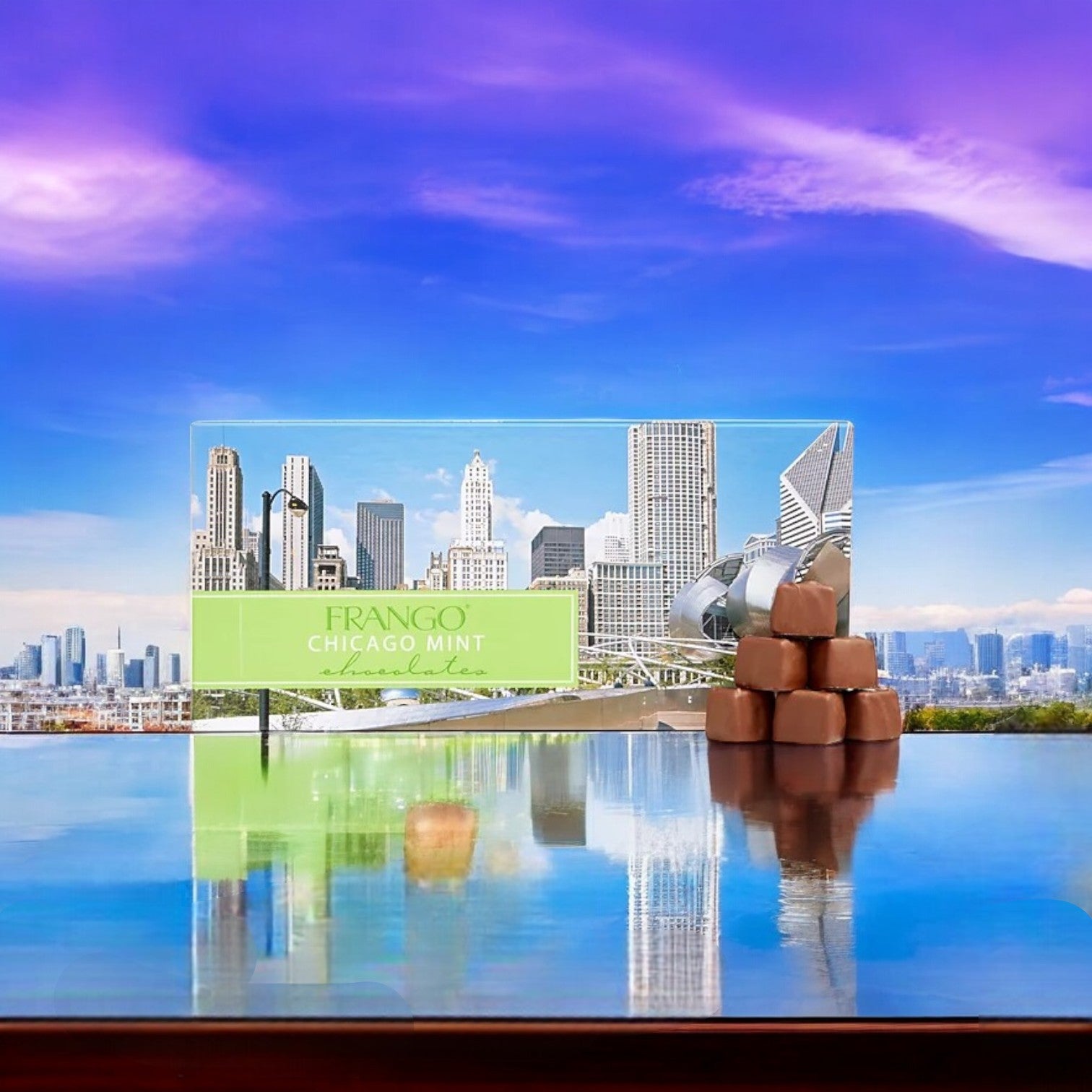 The Garrett Frango Chocolates! Chicago Skyline Milk Mint Box of Chocolate shines on a polished surface with the iconic Chicago skyline beneath a vivid purple sky.