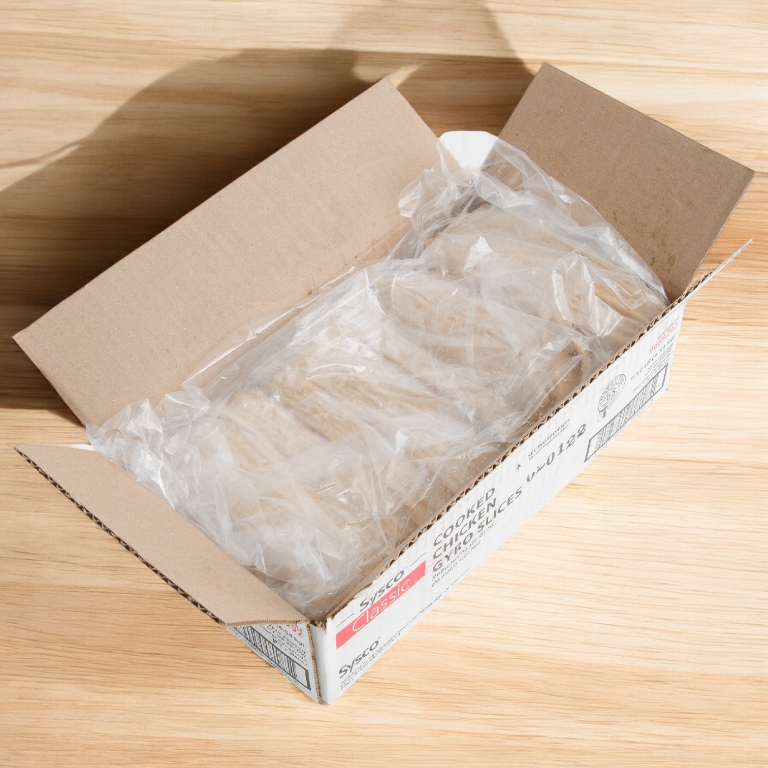 A cardboard box from Sysco Classic rests on a wooden surface, containing transparent plastic packaging with high-quality ingredients to craft Phillip Foods Crab Cake Chesapeake dishes.