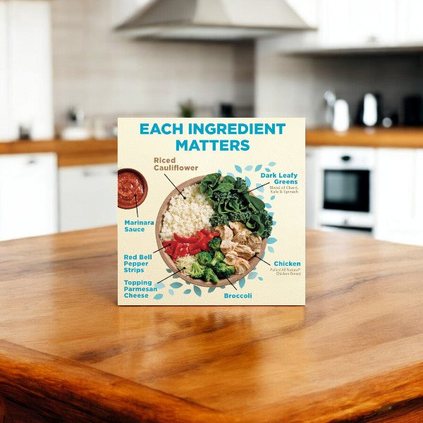 A Healthy Choice Power Bowls Chicken Marinara With Riced Cauliflower package in a kitchen showcases a nutritious meal with riced cauliflower, marinara sauce, red bell pepper strips, Parmesan cheese, dark leafy greens, chicken adobo, and broccoli with the caption "Each Ingredient Matters.