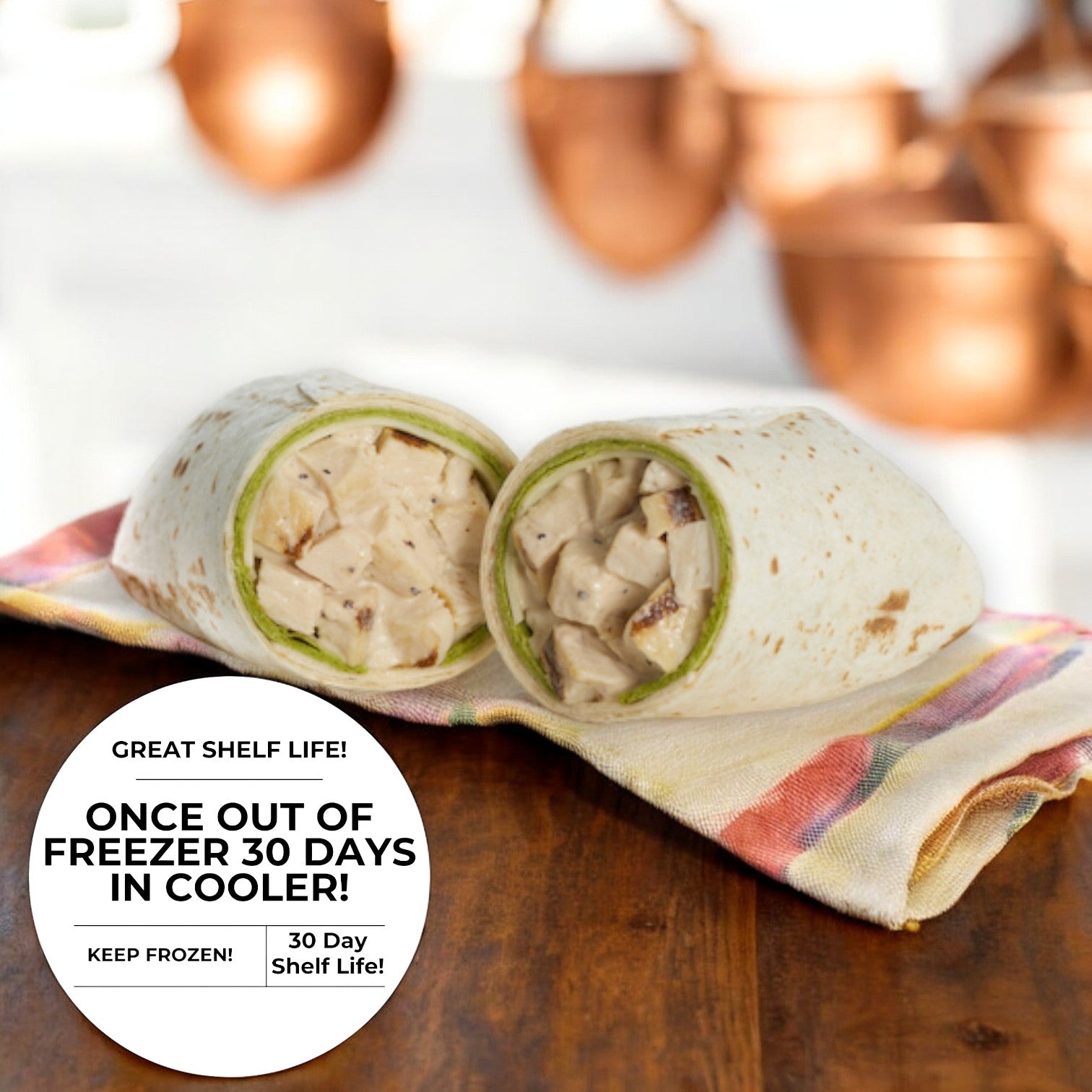 A Chicken Caesar Wrap - 1 Count from E.A. Sween is cut in half and placed on a striped napkin, with text overlay reading, "Great Shelf Life! Once out of the freezer, lasts 30 days in the cooler! Keep frozen! Enjoy a 30-day shelf life!" set against a copper background.