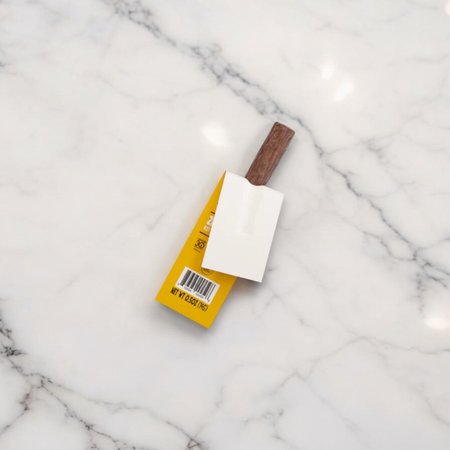 A gluten-free snack of Chomps Mini Antibiotic Free Original Turkey Chomplings, partially wrapped in yellow packaging, lies on a white marble surface.