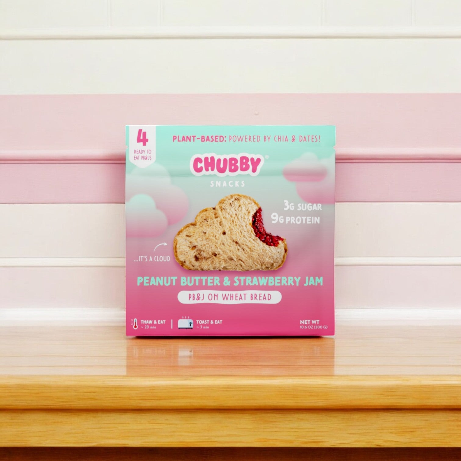 A bag of Chubby's Peanut Butter & Strawberry Jam, featuring four 2 oz superfood sandwiches, sits on a wooden surface against a pink and white background, providing a convenient snack rich in protein and fiber.