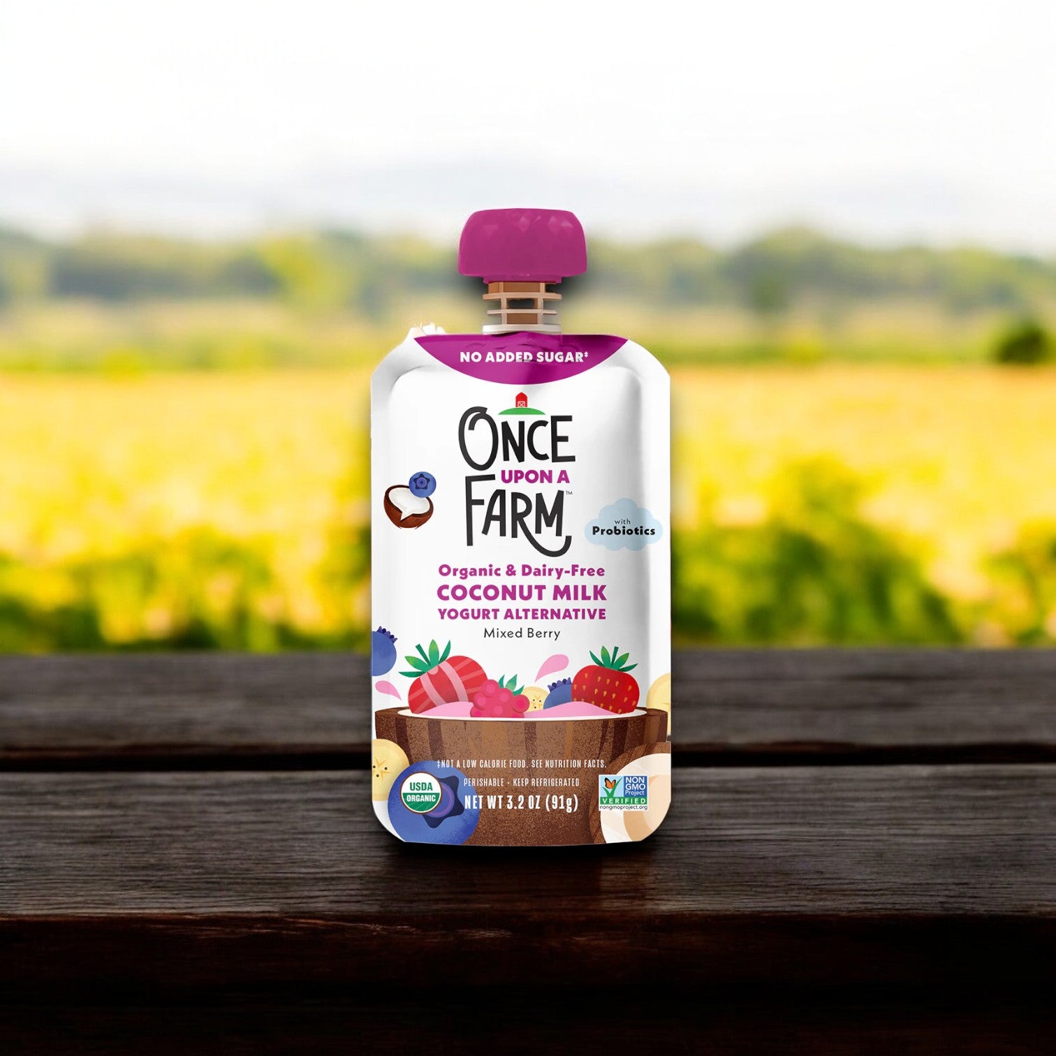 A pouch of Once Upon a Farm Mixed Berry Coconut Milk Yogurt, resting on a wooden surface with a blurred outdoor background.