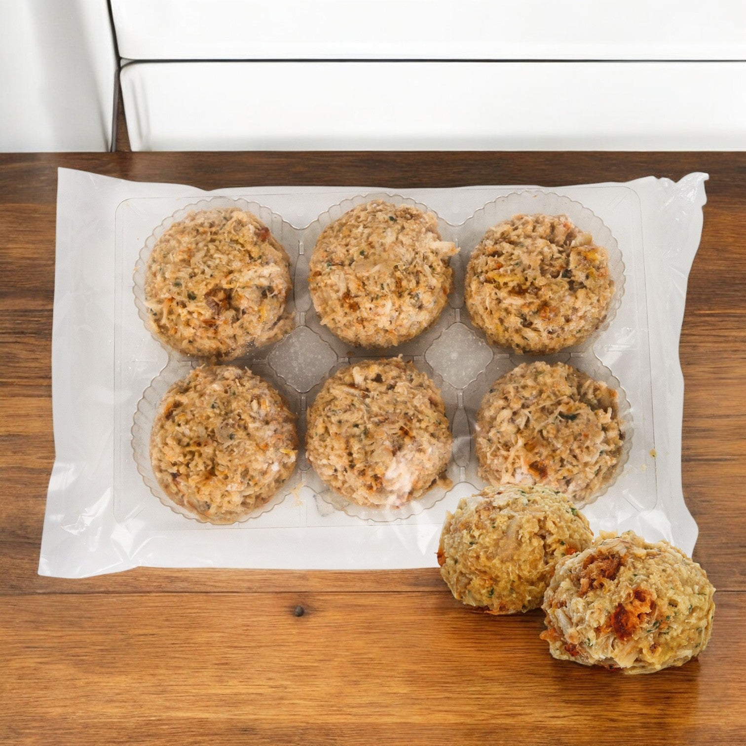 A vacuum-sealed package of six stuffing balls, accompanied by two more unwrapped ones on a wooden surface, delivers the genuine Chesapeake flavor reminiscent of Phillips Foods Crab Meat Culinary Jumbo Pasteurized Asian taste, echoing the essence of wild-caught crab meat.