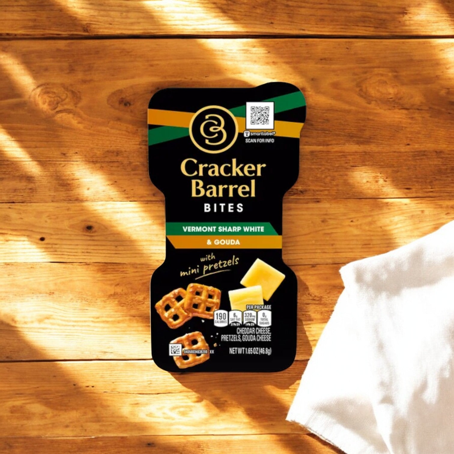 A 1.59 oz package of Easy Lunches' Cracker Barrel Bites with Vermont Sharp White Cheddar and Gouda Cheese with Pretzel Chips, placed on a wooden surface with a white cloth partially visible on the side.