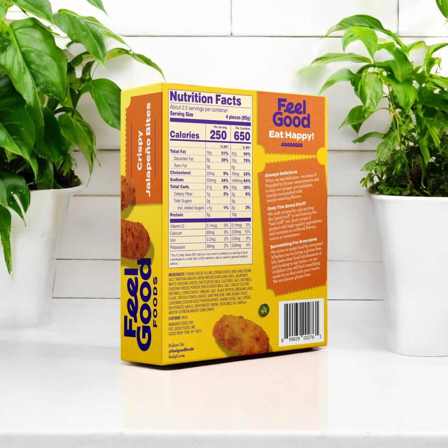 On a white table sits the back of a Feel Good Foods, Crispy Jalapeno Bites box, showcasing nutrition facts and text, surrounded by lush green plants in the background. Savor the irresistible crunch and savory delight of our spicy jalapeno filling in every bite.