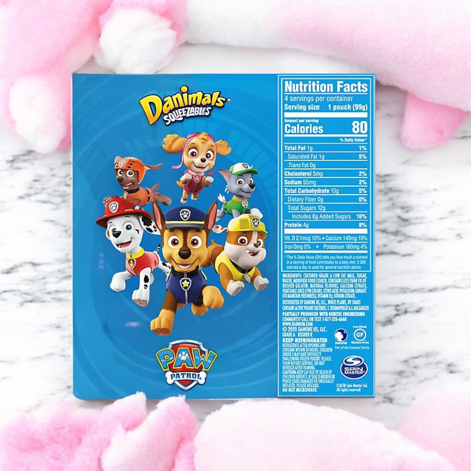 Blue package of Easy Lunches Danimals Cotton Candy Squeezable Yogurt - 3.5 oz - 4 Pack, featuring PAW Patrol characters and a nutrition facts label on the back. The package is surrounded by pink stuffed animal paws on a white background, emphasizing its rich calcium and Vitamin D content.