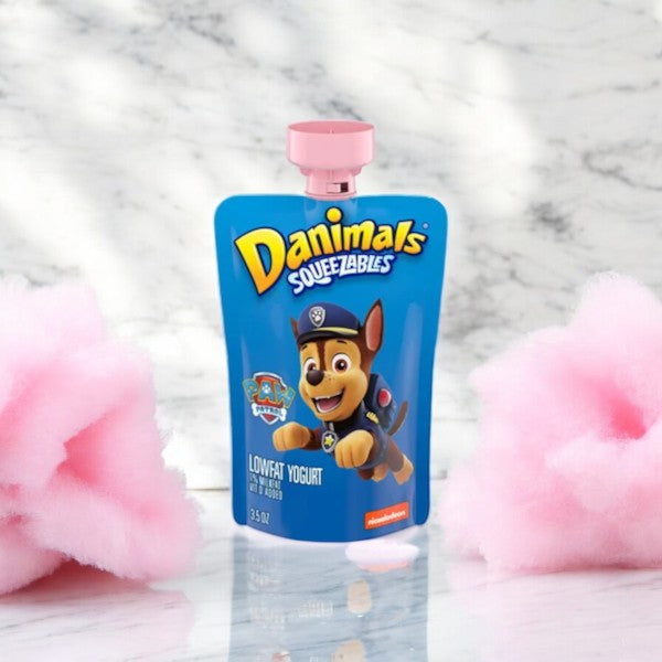 A 3.5 oz pouch of Danimals Cotton Candy Squeezable Yogurt from the Easy Lunches brand, featuring a cartoon dog in a police uniform against a backdrop of pink cotton candy on a marble background. This low-fat yogurt pouch is perfect for a convenient and nutritious snack.