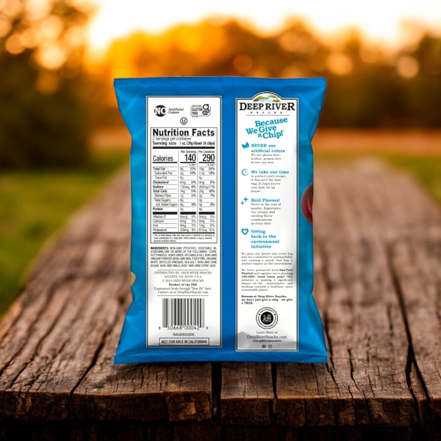 Back of a blue bag of Deep River Snacks Salt & Vinegar Kettle Potato Chips on a wooden table with a blurred outdoor background, showcasing nutritional info and text highlights, including its gluten-free promise.