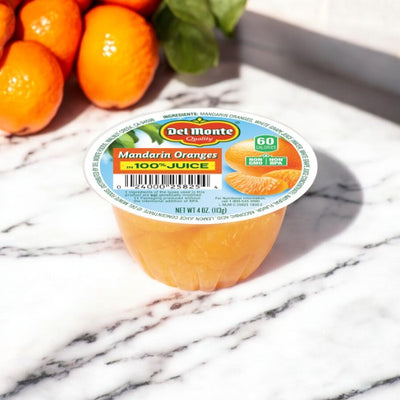 A Del Monte Mandarin Oranges Fruit Cup, No Sugar Added, 4 oz - 1 Count is displayed on a marble surface background, with a few whole non-GMO mandarin oranges partially visible in the top left corner.