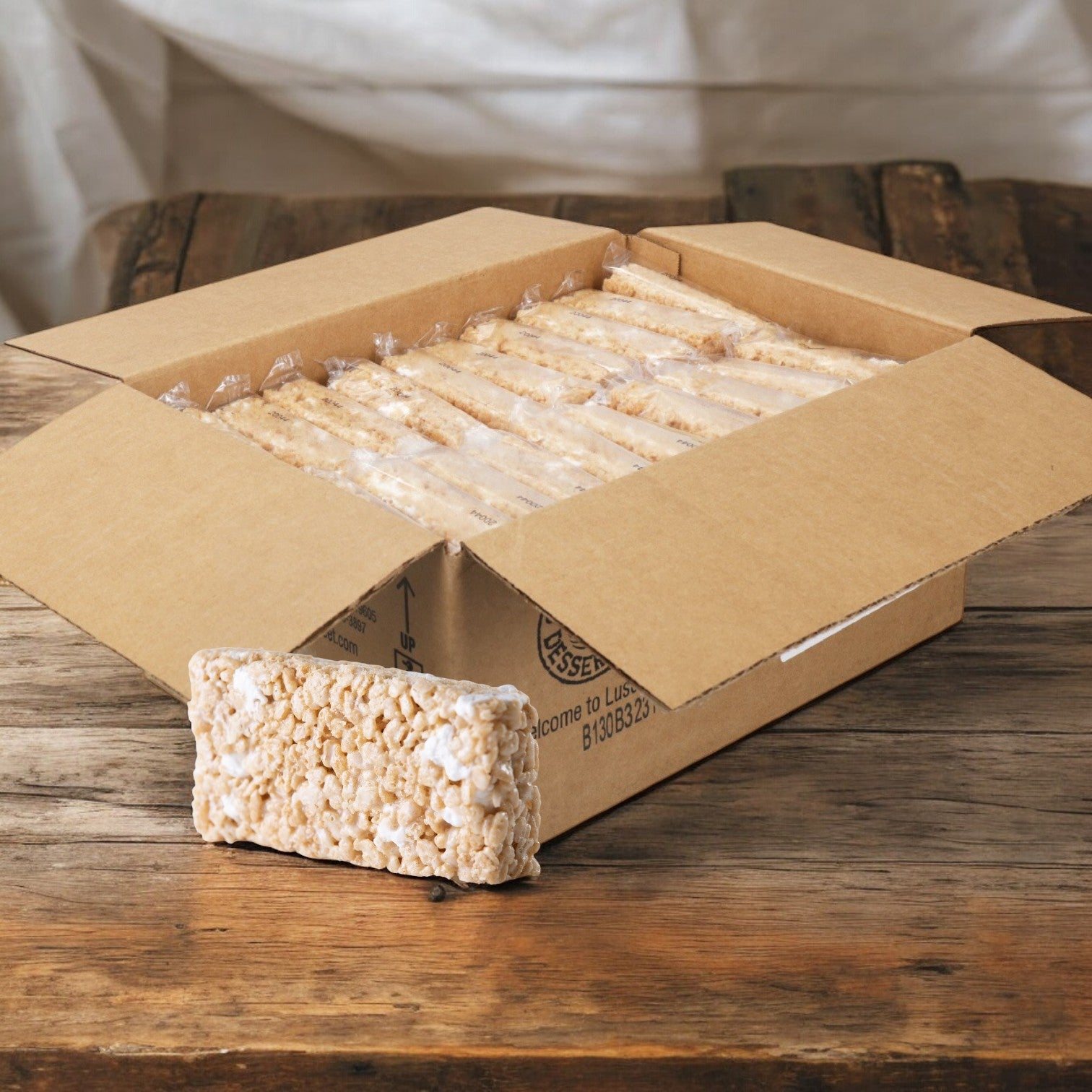 A box of Sweet Street Dessert Bar Marshmallow treats, 2.1 oz each and individually wrapped, sits on a wooden table with one chewy bar partially pulled out.