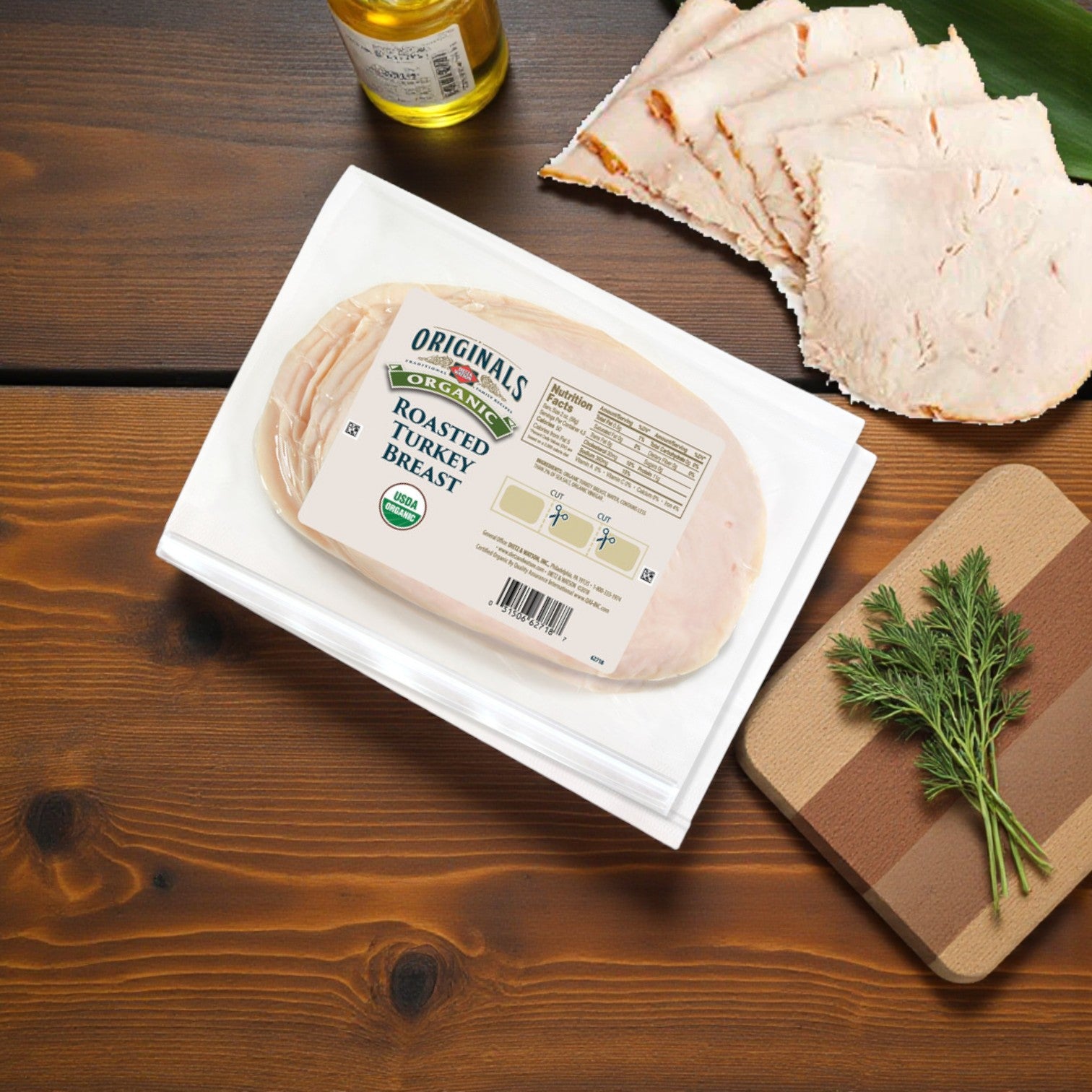 Dietz & Watson Organic Roasted Turkey Breast – 9 oz, 3 Count, packaged and sliced nitrate free deli meat on a wooden table with fresh herbs and a bottle on a small cutting board nearby.