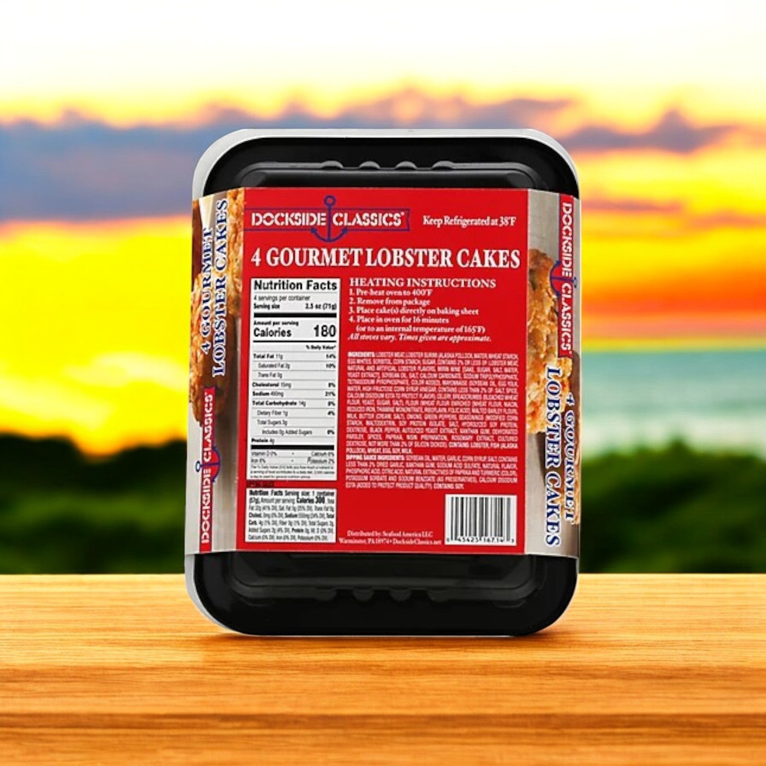 A 10 oz. package of Dockside Classics Premium Lobster Cakes, made with high-quality ingredients, includes nutrition information and cooking directions against a blurred outdoor sunset backdrop to enhance the gourmet dining experience.