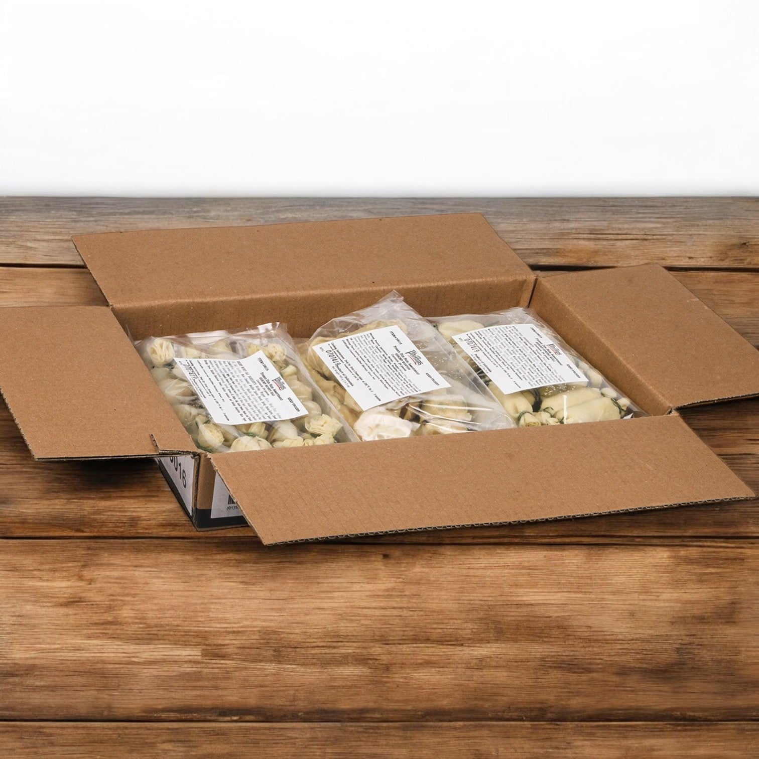An open cardboard box rests on a wooden surface, showcasing several sealed plastic bags filled with Phillip Foods Dim Sum Fried appetizers—72 light-colored mini claw crab cakes in total, perfect for any occasion.