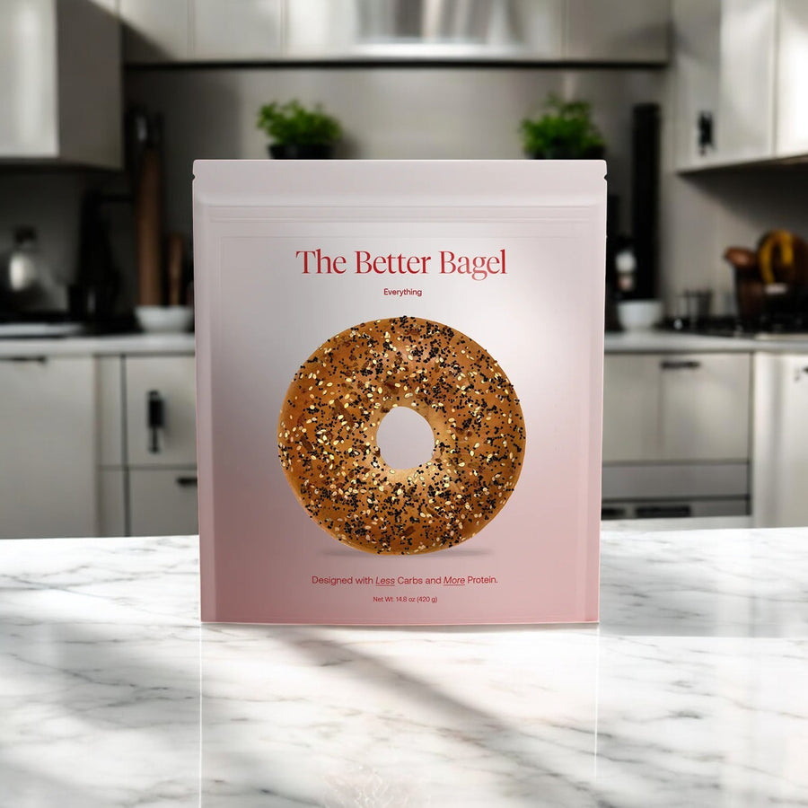A package labeled “Better Brand - The Everything Better Bagel” (1 bag, 4 bagels) with high protein, low carb everything bagels sits on a marble countertop in a modern kitchen; in stock and ready to ship from BetterBrand.