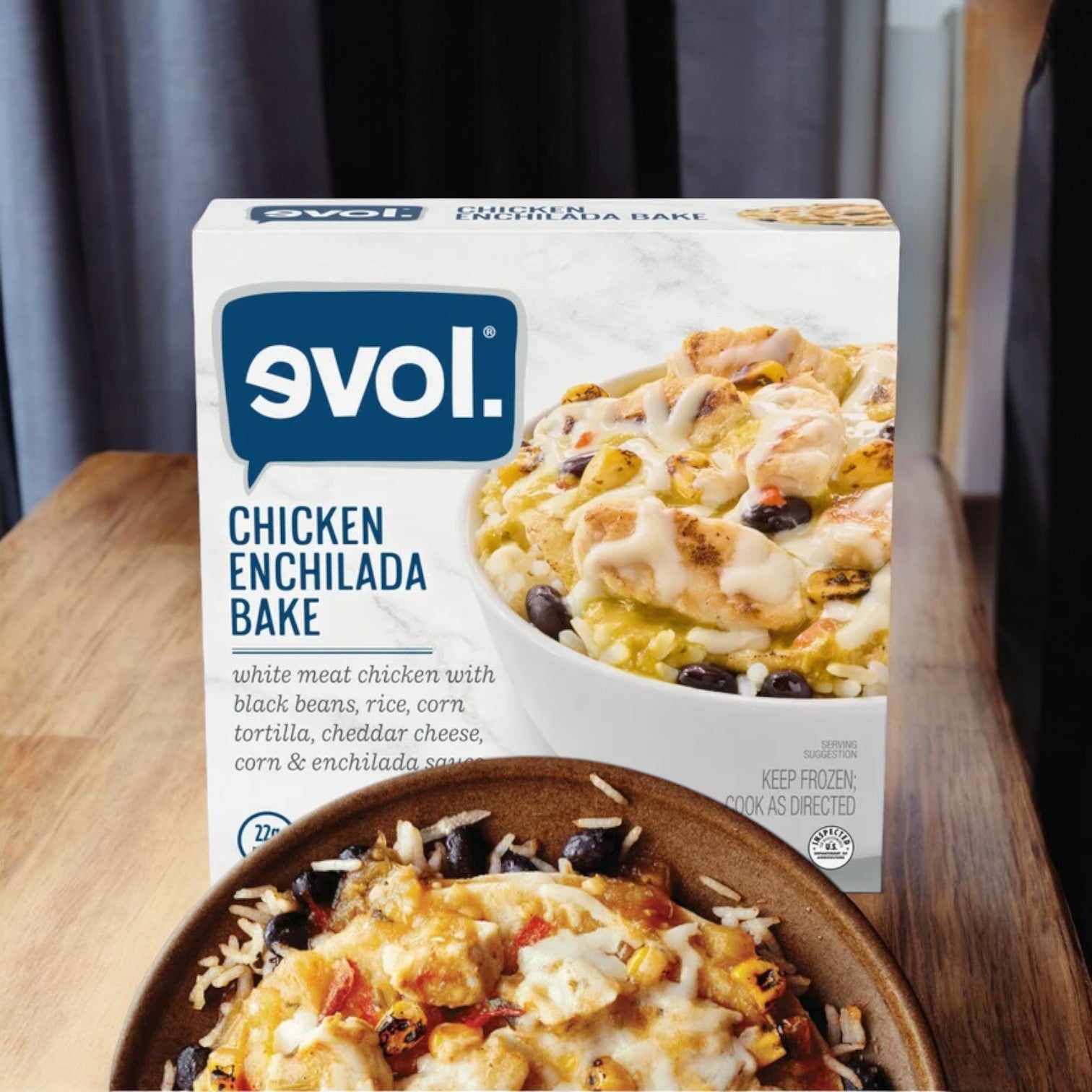 A box of Evol Chicken Enchilada Bake, Gluten Free, 9 oz. - 1 Count, sits on a wooden surface, with the delicious prepared meal in a bowl in front of it.