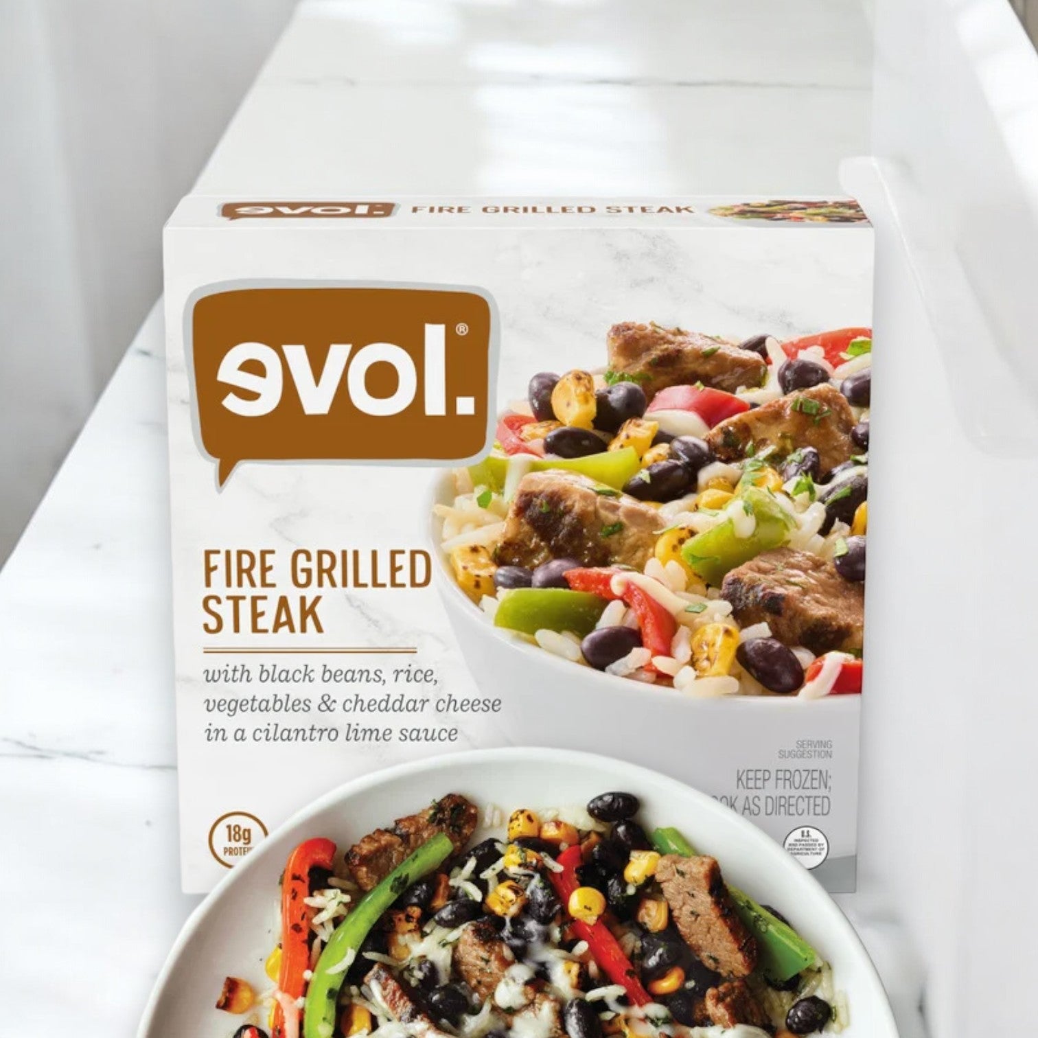 The packaging for "Evol Gluten Free Fire Grilled Steak, 9 oz. - 1 Count" by Evol is displayed behind a bowl containing the prepared dish, which features steak, black beans, rice, vegetables, and cheddar cheese in a cilantro lime sauce for a gourmet experience.