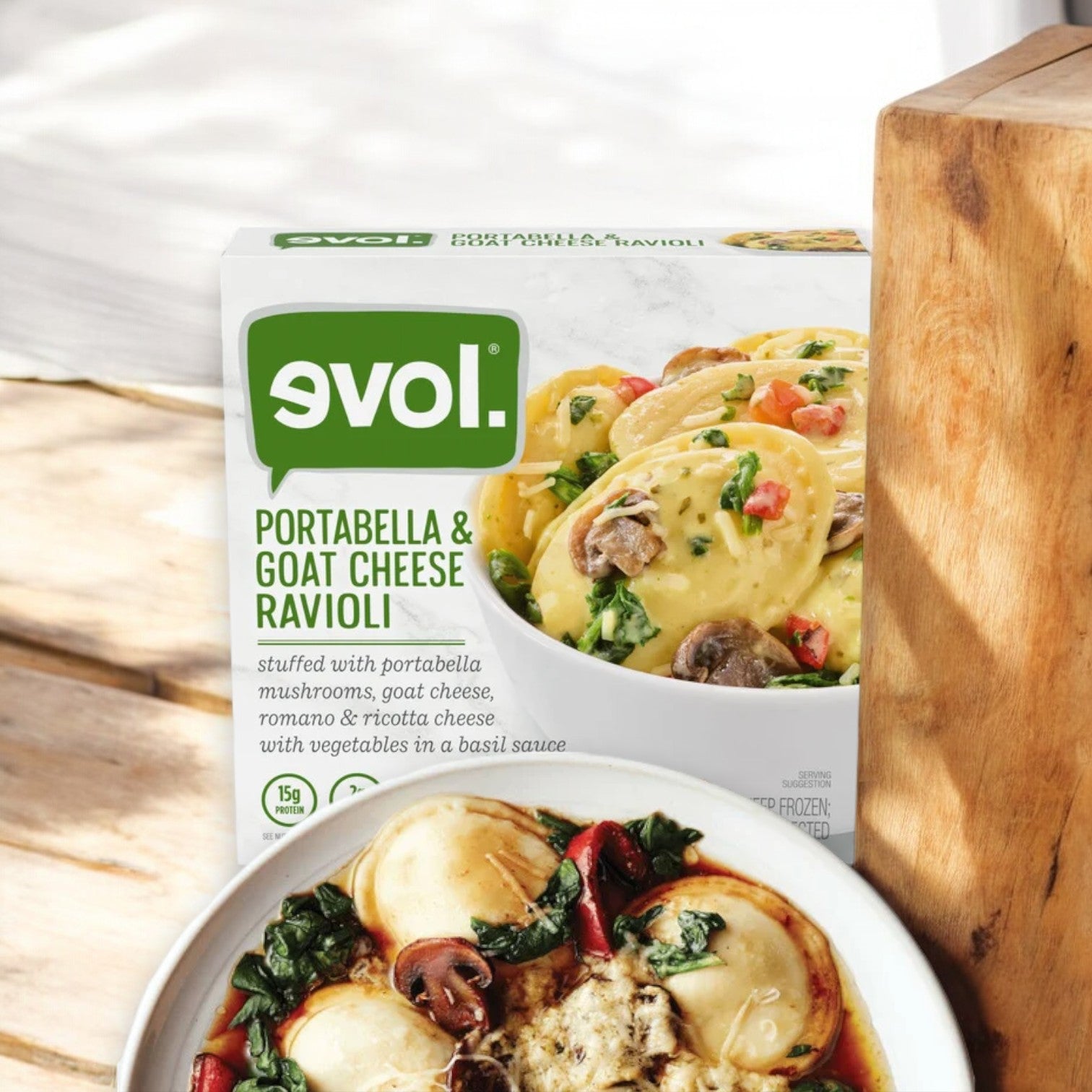 A box of Evol Portabella & Goat Cheese Ravioli, 8.75 oz. - 1 Count is placed next to a plate of cooked ravioli with vegetables in a basil sauce.