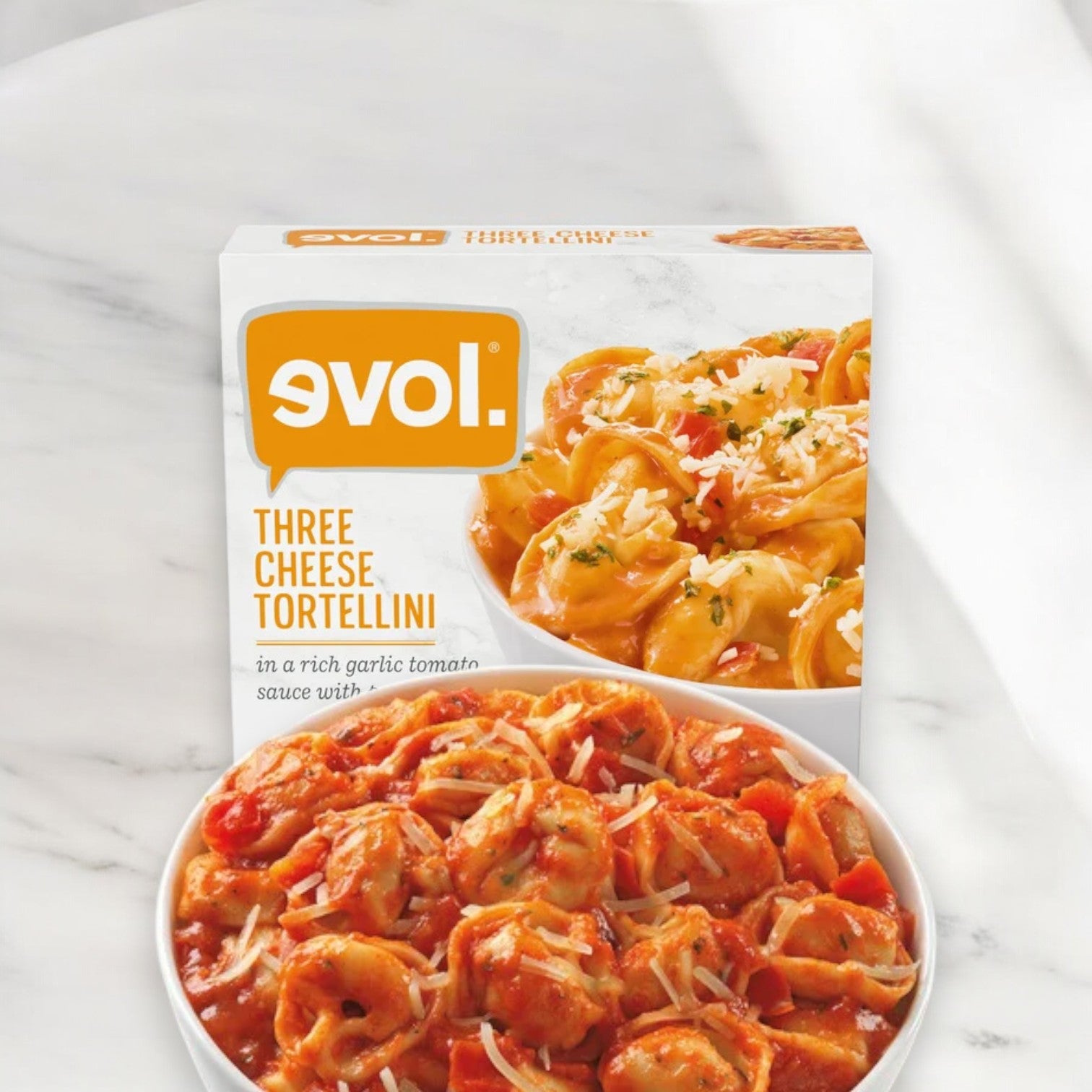 A box of Evol Three Cheese Tortellini, 9 oz. - 1 Count is shown with the cooked dish displayed in a bowl below, featuring tortellini in a rich garlic tomato sauce topped with grated cheese—a hearty meal perfect for any occasion.