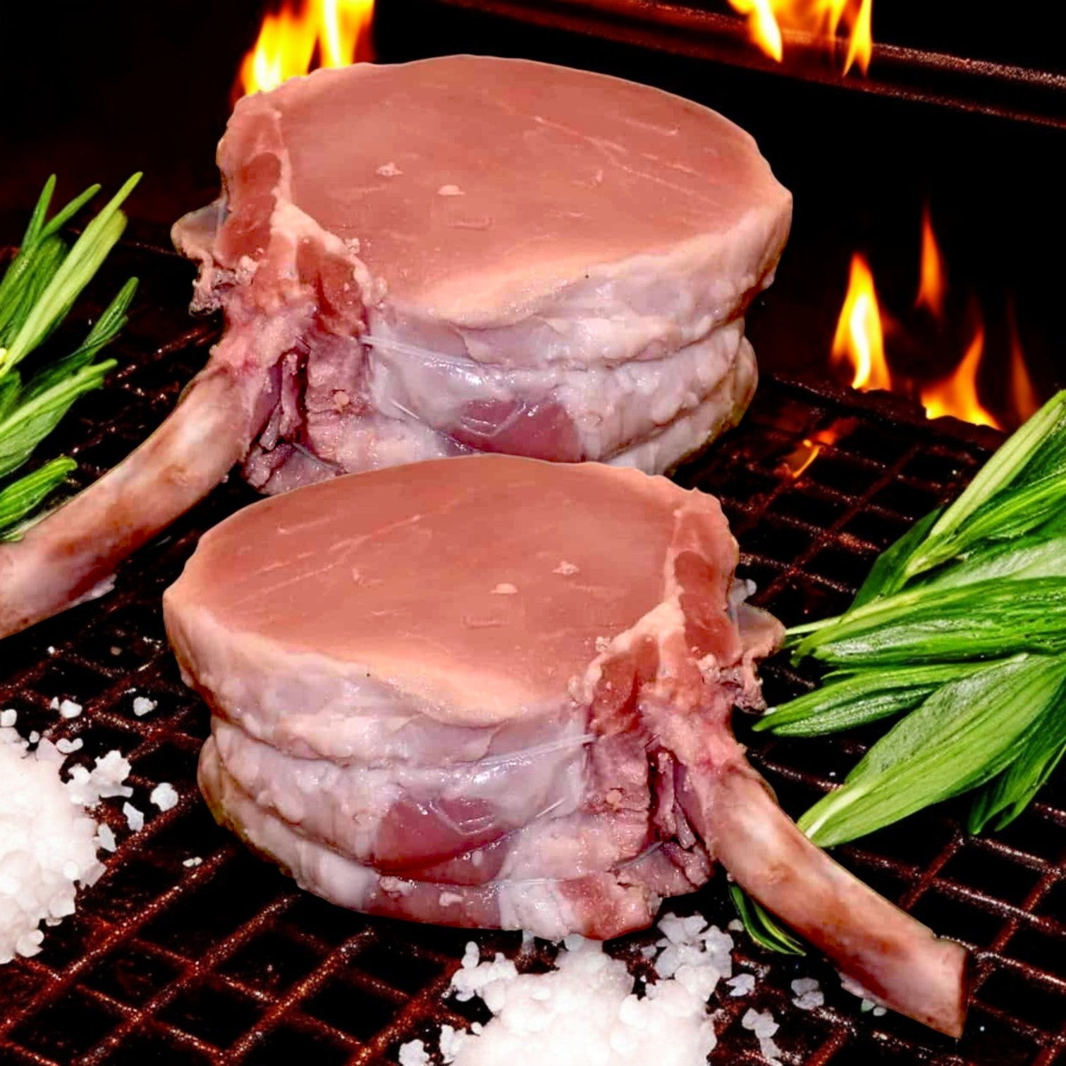 Two raw, premium-cut pork chops from the Mino Prime Steaks - Top Seller Box on a grill with flames, garnished with rosemary and surrounded by coarse salt.