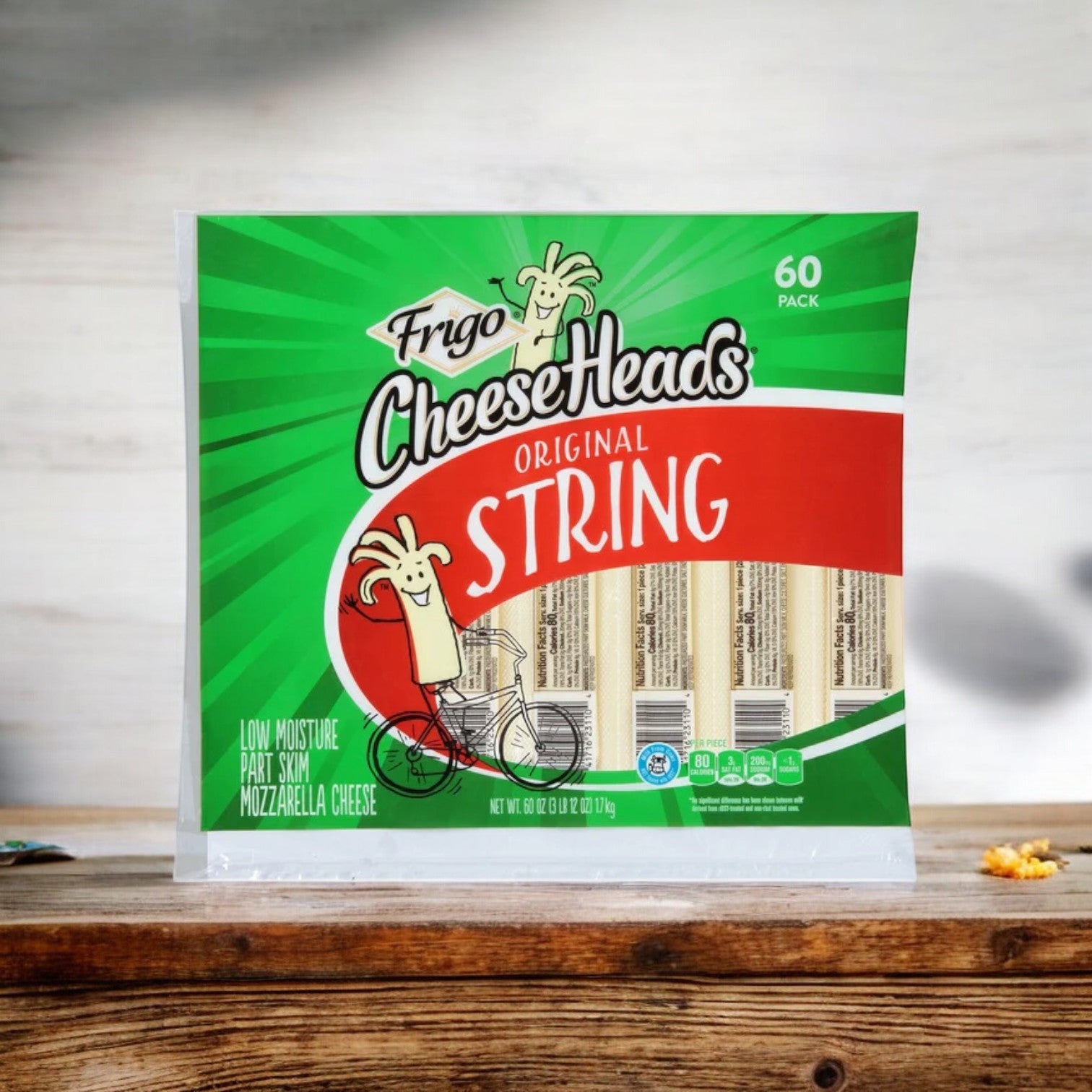 A pack of Frigo® Cheese Heads® Original Mozzarella String Cheese snacks sits on a wooden table, featuring a cartoon cheese character on a bicycle. This high-protein, low-calorie mozzarella treat is perfect for any time of day.
