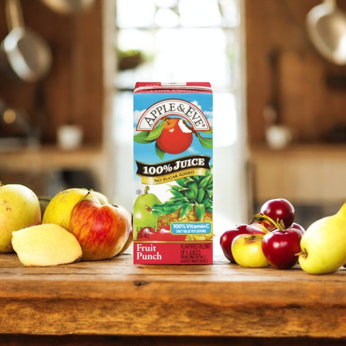 A carton of Adam and Eve Apple Juice, Fruit Punch Flavor (6.75 fl oz - 1 Count) from Apple & Eve sits on a wooden table surrounded by apples, cherries, and a pear, with a blurred kitchen background. This healthy beverage offers natural flavor, delivering the perfect blend of fruit punch for any occasion.