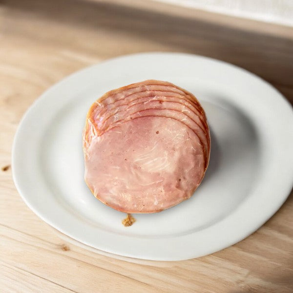 A sliced piece of Applegate Natural Uncured Black Forest Ham, 7 oz - 1 Count, is placed on a white plate on a wooden surface.